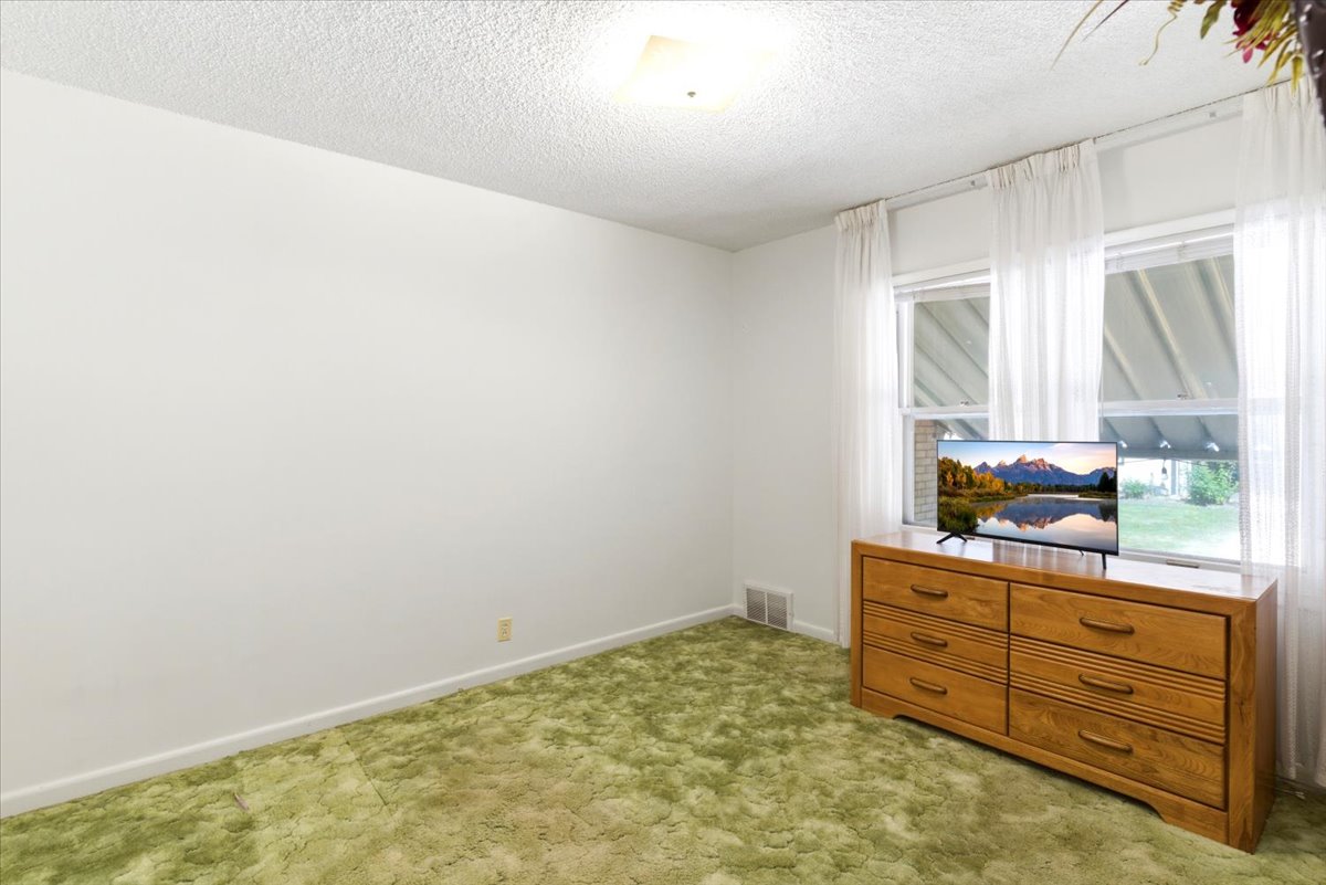 Well-lit room featuring multiple windows, textured ceiling, light green carpet flooring, and white walls with baseboards
