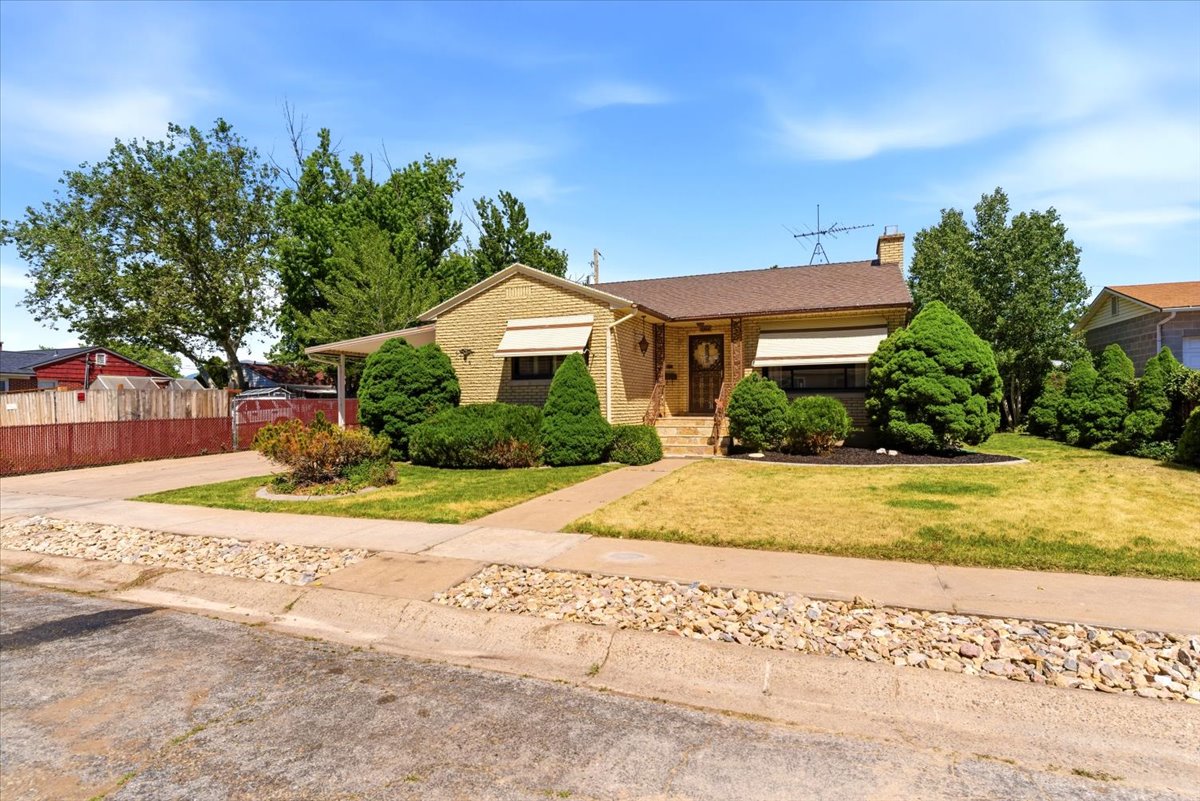 Single-story brick exterior featuring a covered front porch, an extended driveway, mature landscaping, and a fenced side yard