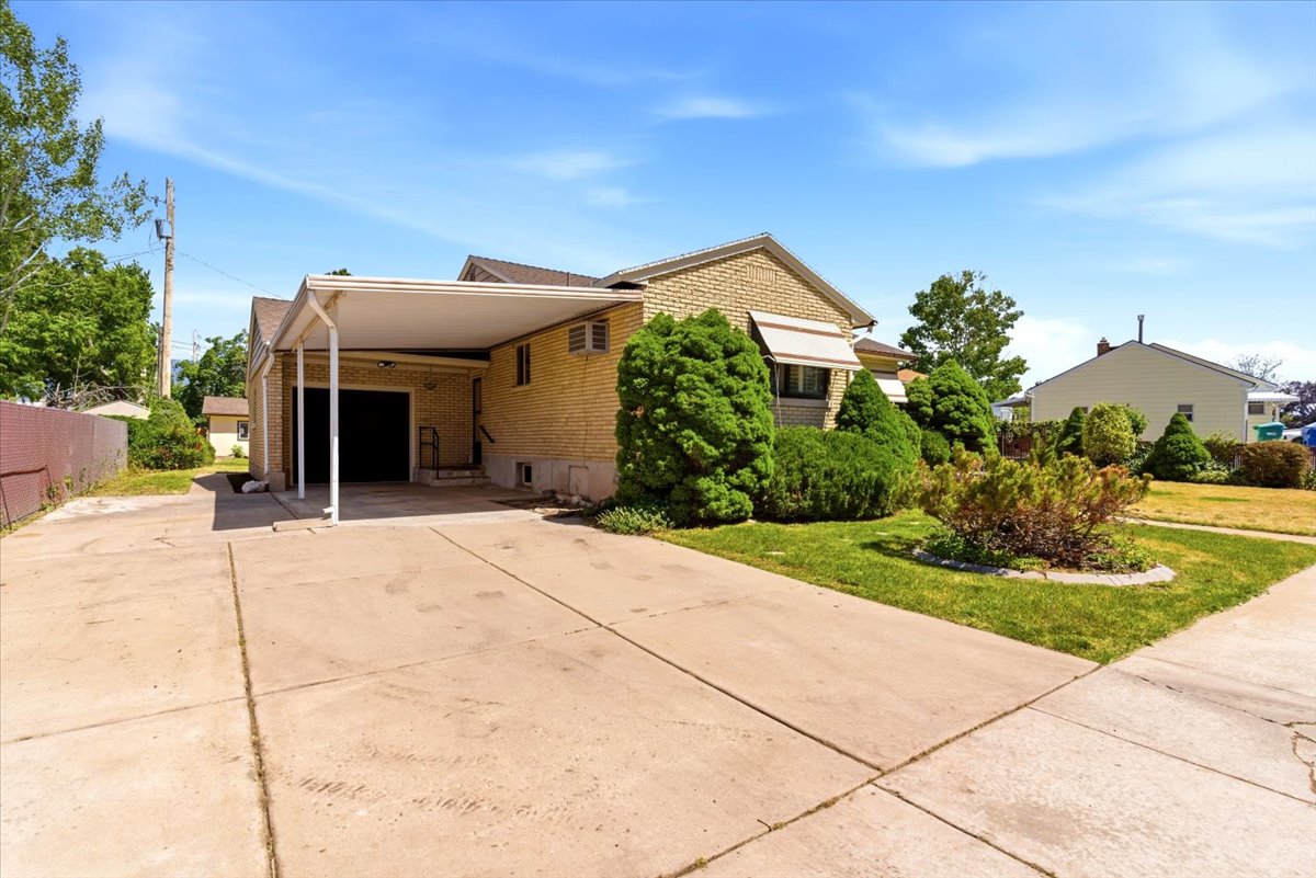 Brick exterior featuring an attached carport, an extended concrete driveway, and established front yard landscaping