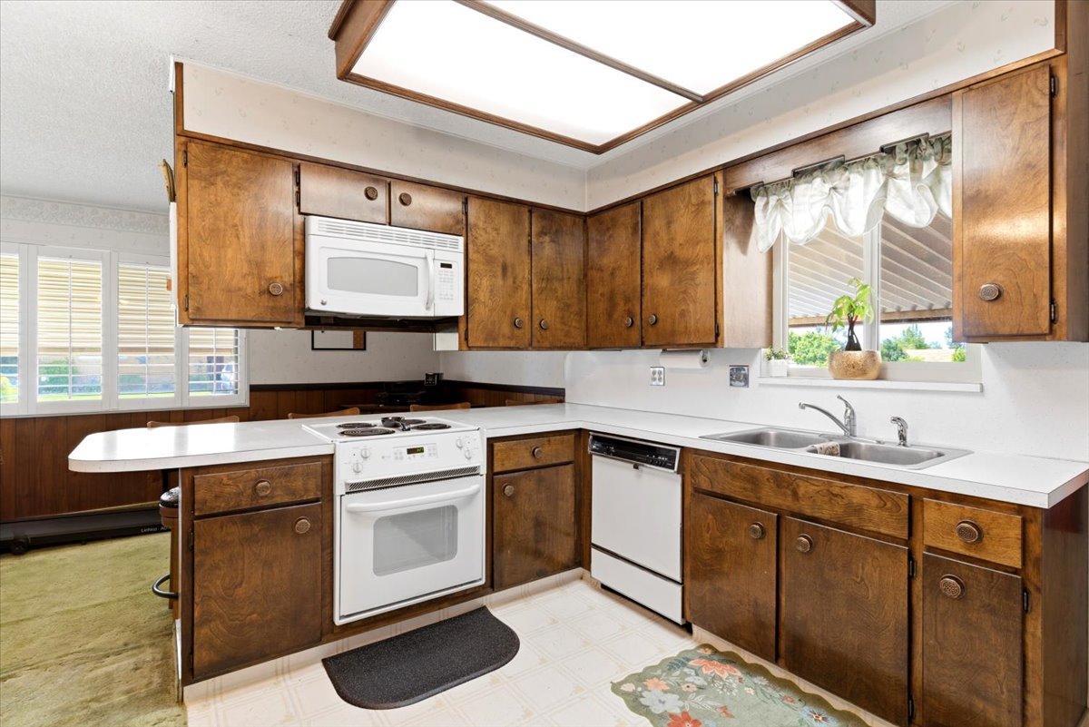 Corner kitchen featuring wood cabinetry, white countertops, a built-in microwave, a white electric range, and a double basin sink