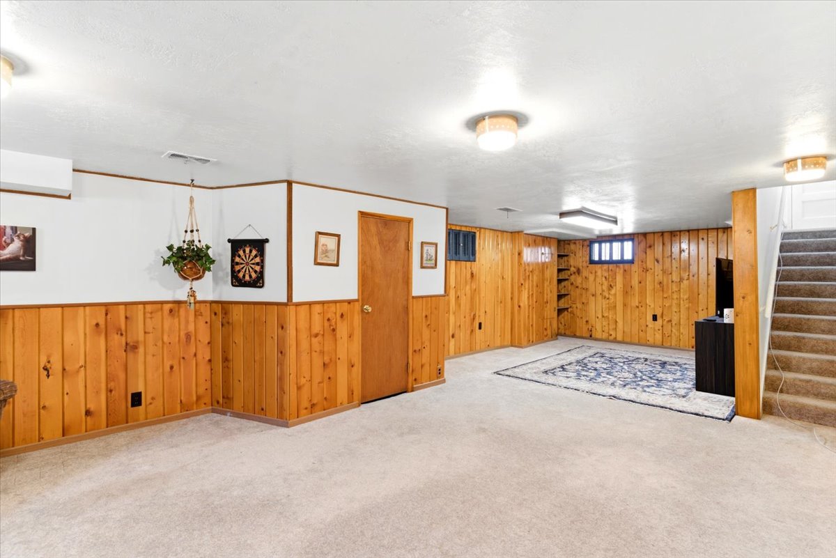 Spacious room featuring carpeting, wood paneling, white painted walls, and built-in shelving