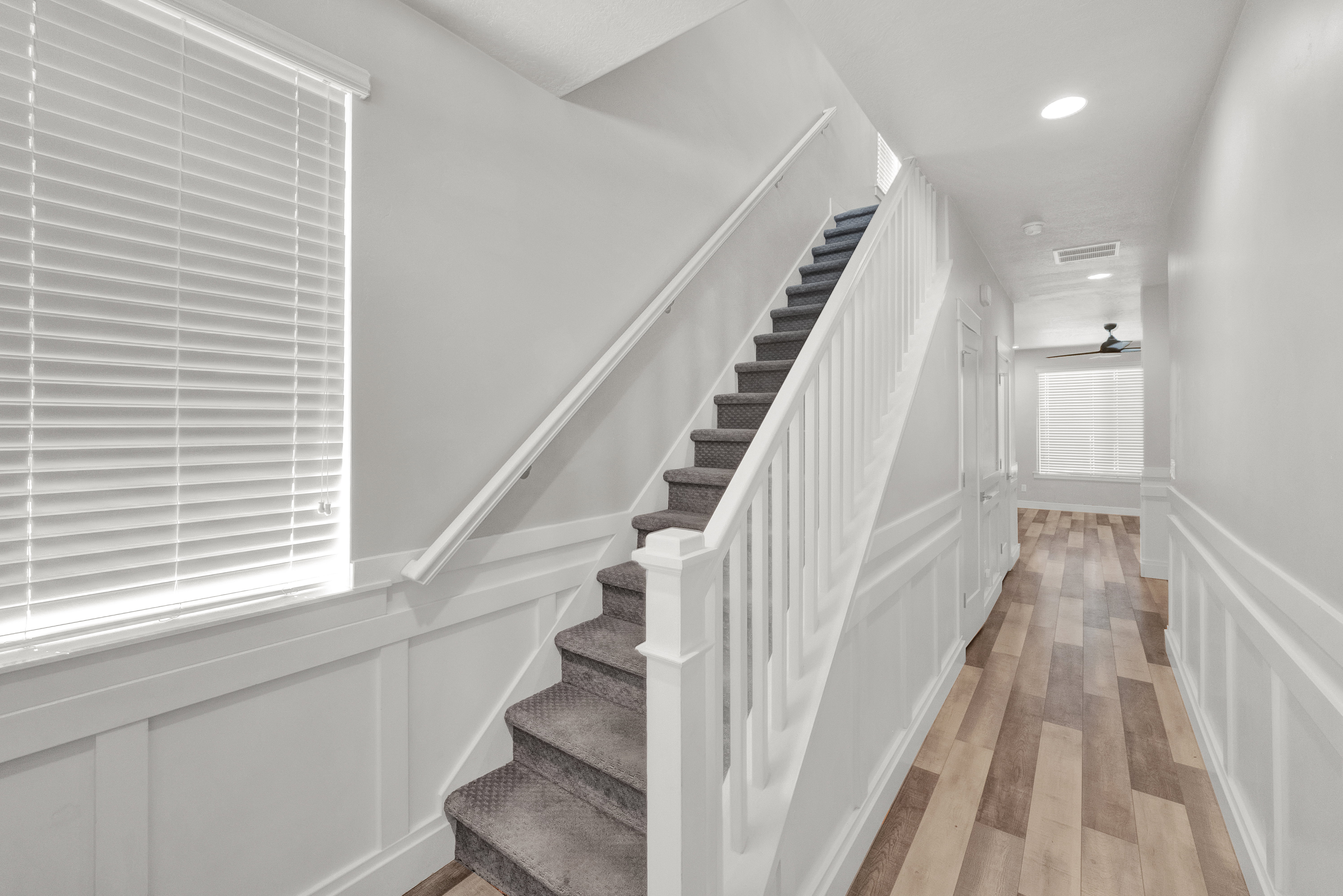 Carpeted staircase with white balusters and handrail, featuring wainscoting, wood-finish flooring, recessed lighting, and a ceiling fan