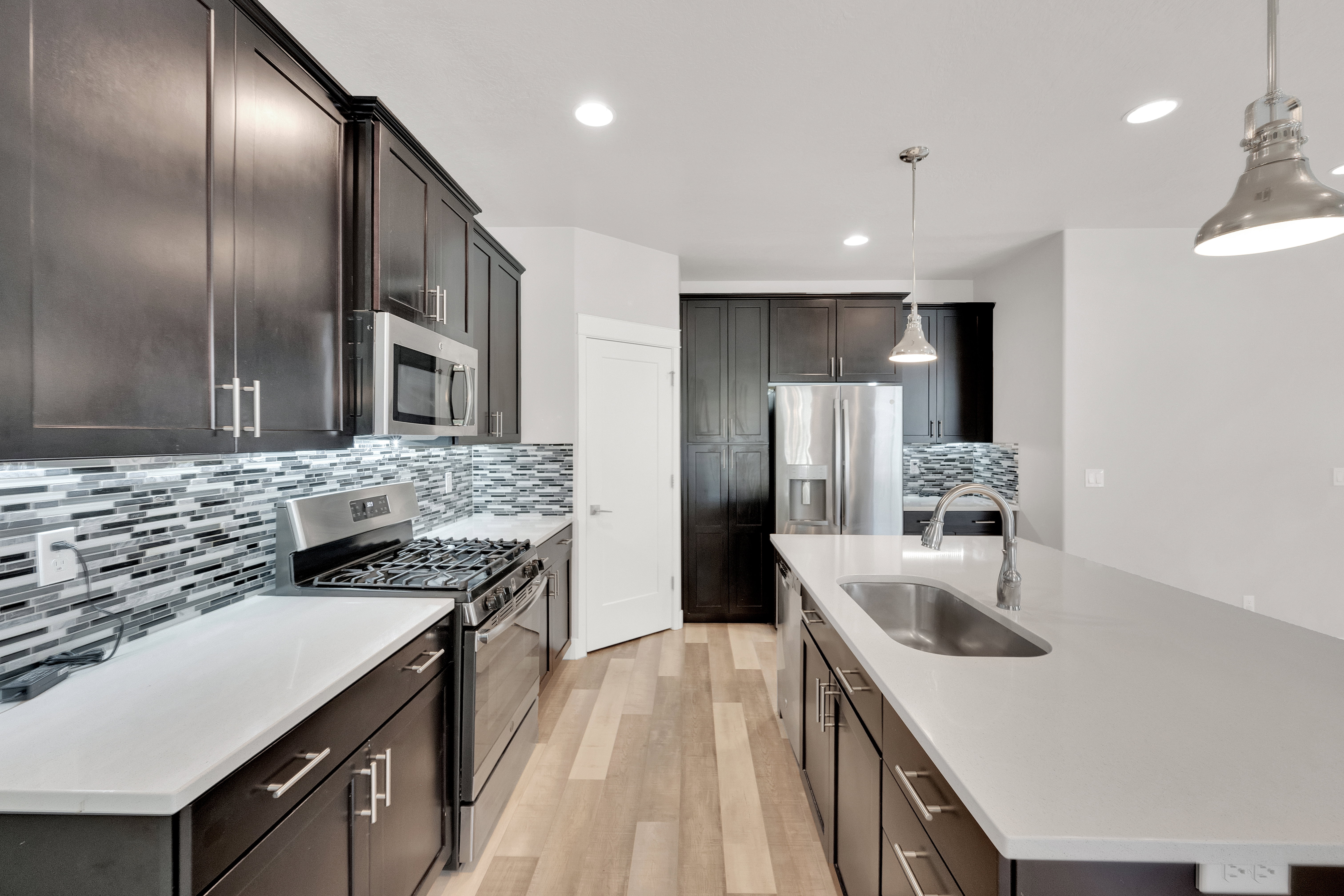 Modern kitchen featuring dark wood-finish cabinetry, stainless steel appliances, light-toned countertops, and a full-height mosaic tile backsplash