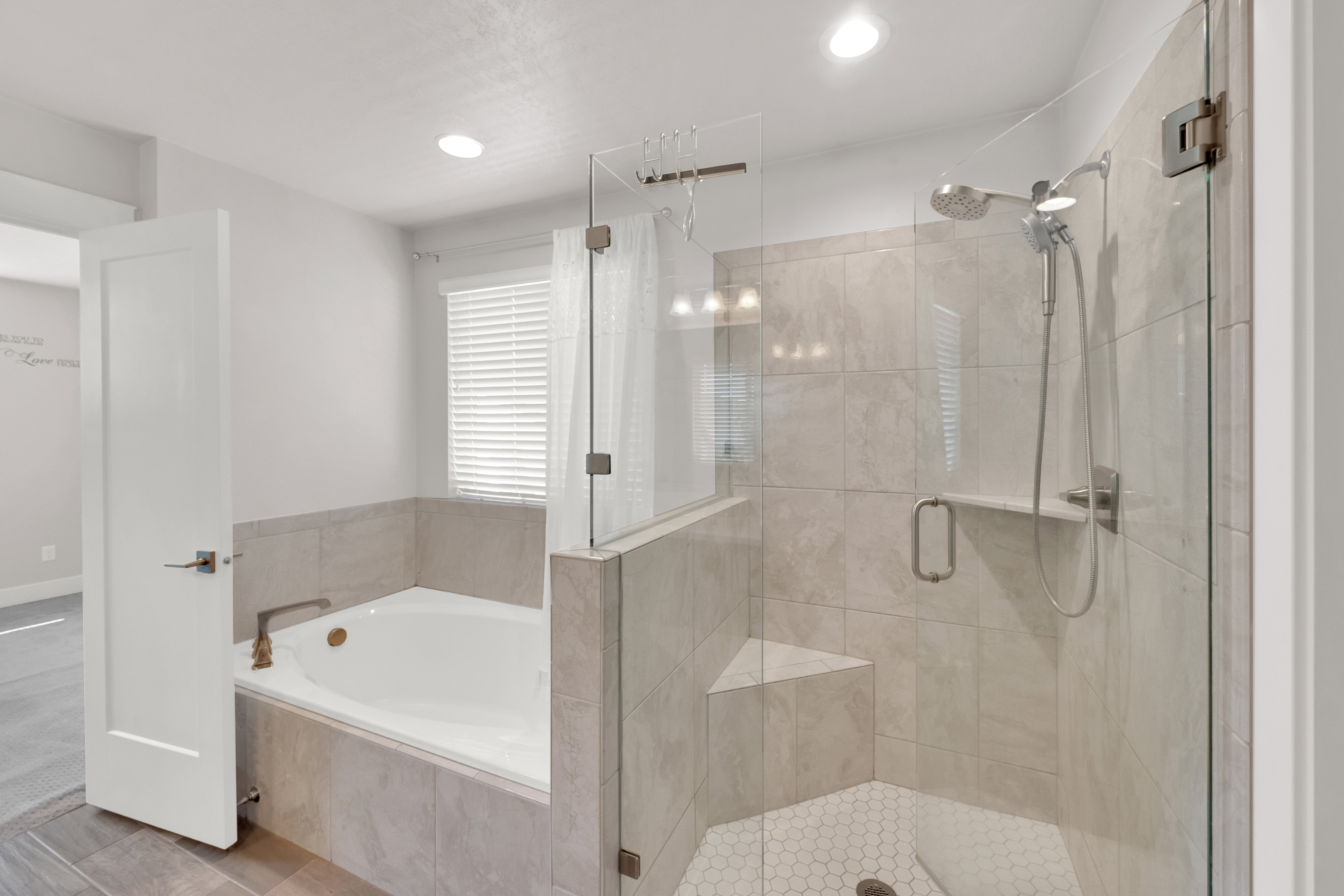 Spacious bathroom featuring a built-in soaking tub with a tiled surround, a separate glass-enclosed shower with a built-in bench, a handheld showerhead, and light-toned tile flooring