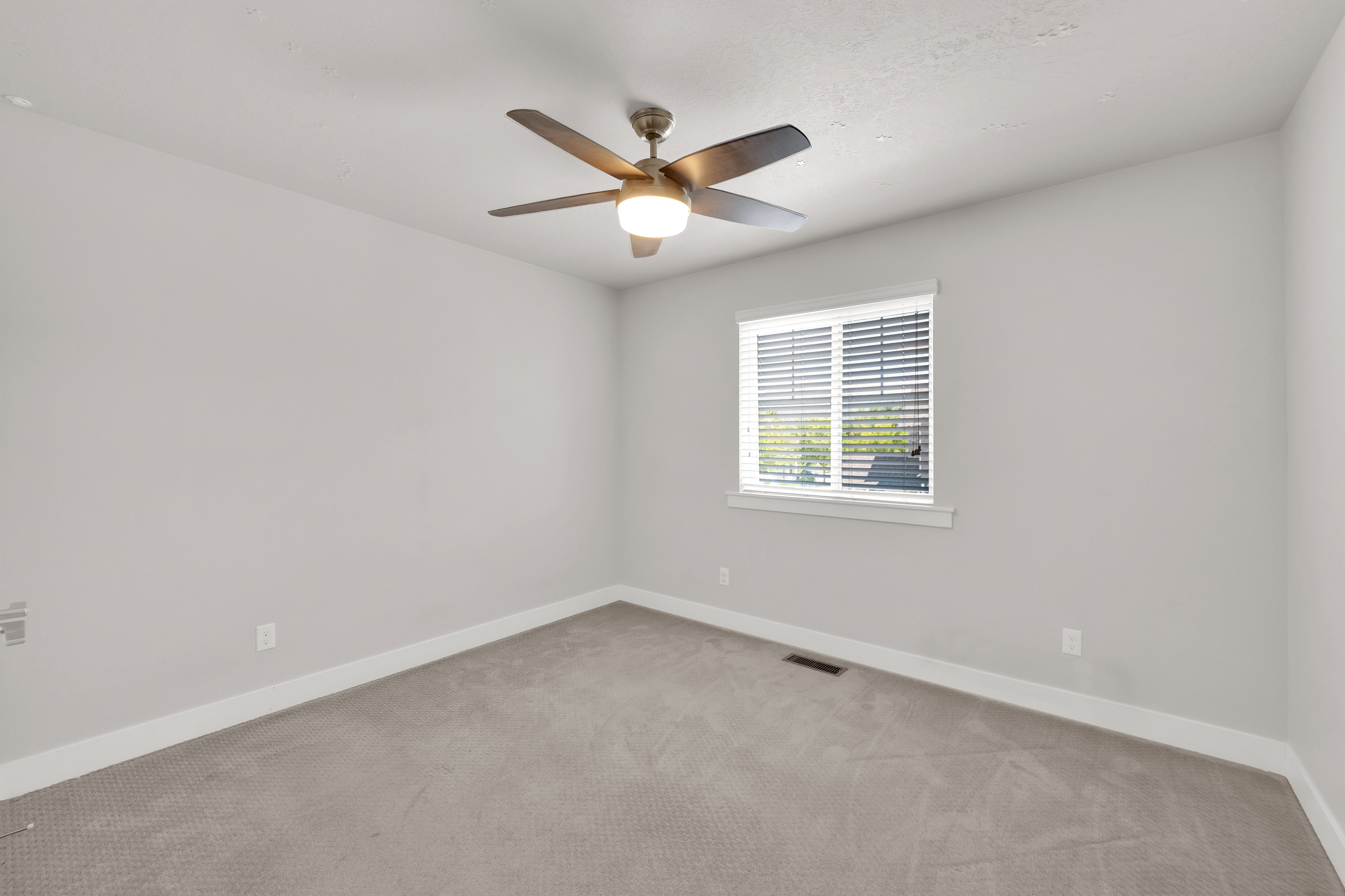 Neutral-toned room featuring a ceiling fan with integrated lighting, a window with horizontal blinds, gray textured carpeting, and white baseboards