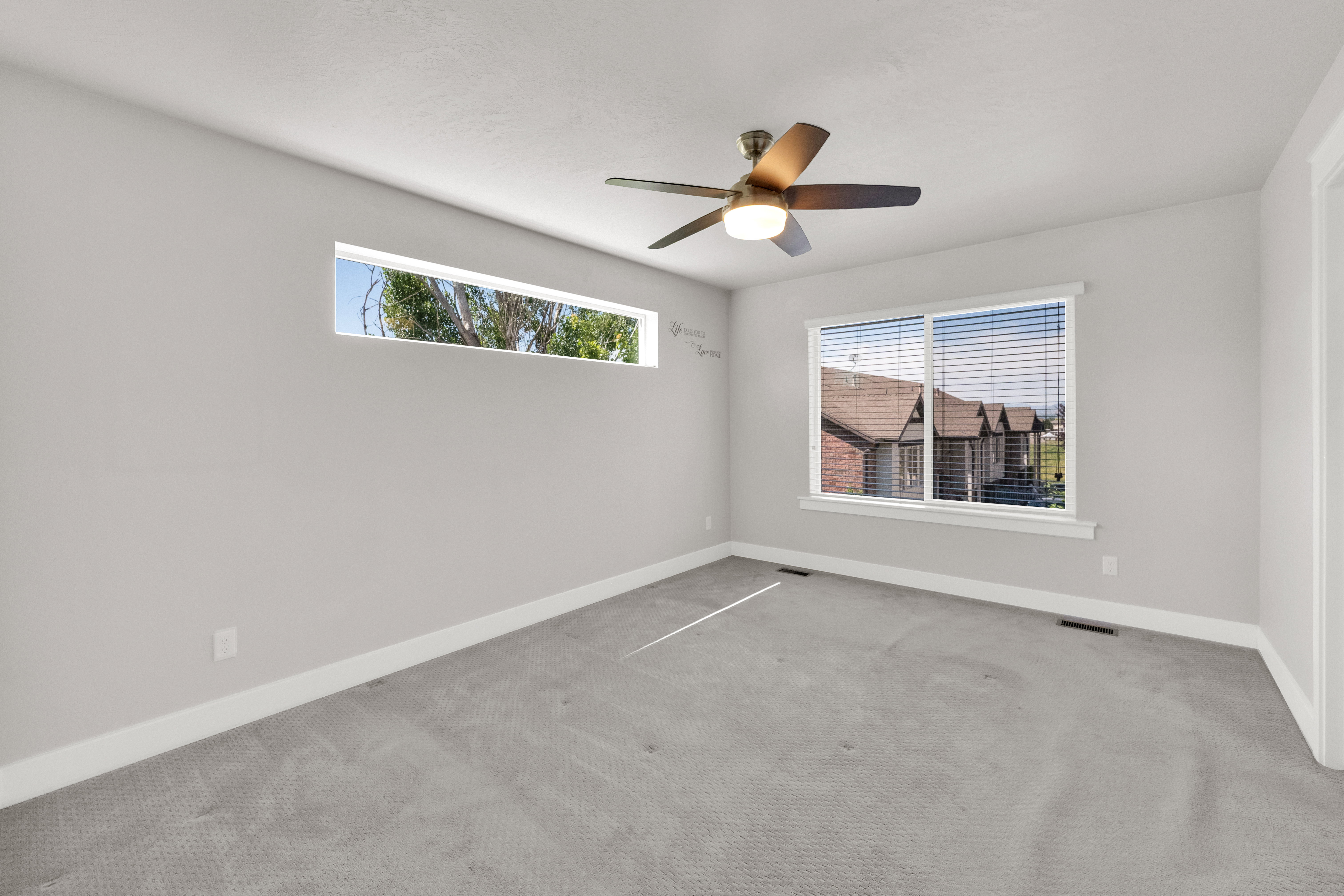 Spacious room featuring light gray walls, plush gray carpeting, and white baseboards