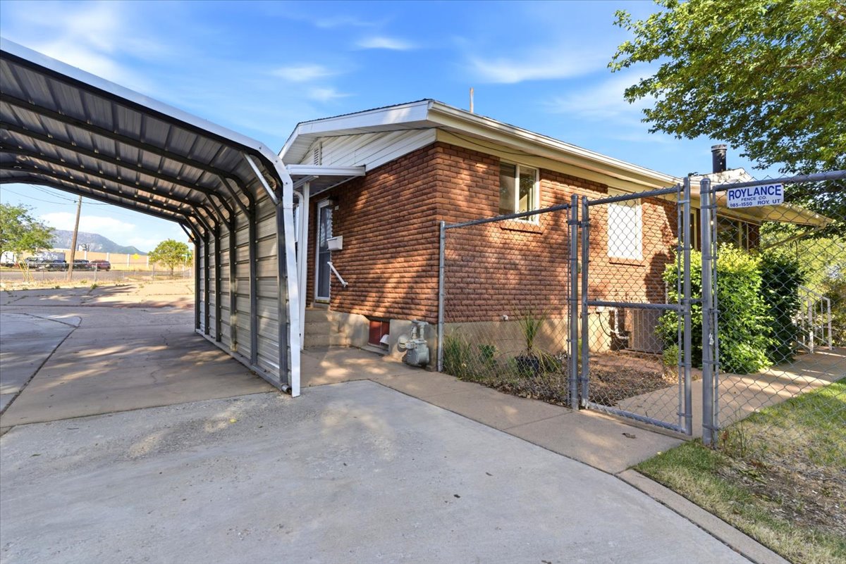 Brick exterior featuring a covered carport, concrete driveway, and chain-link fencing
