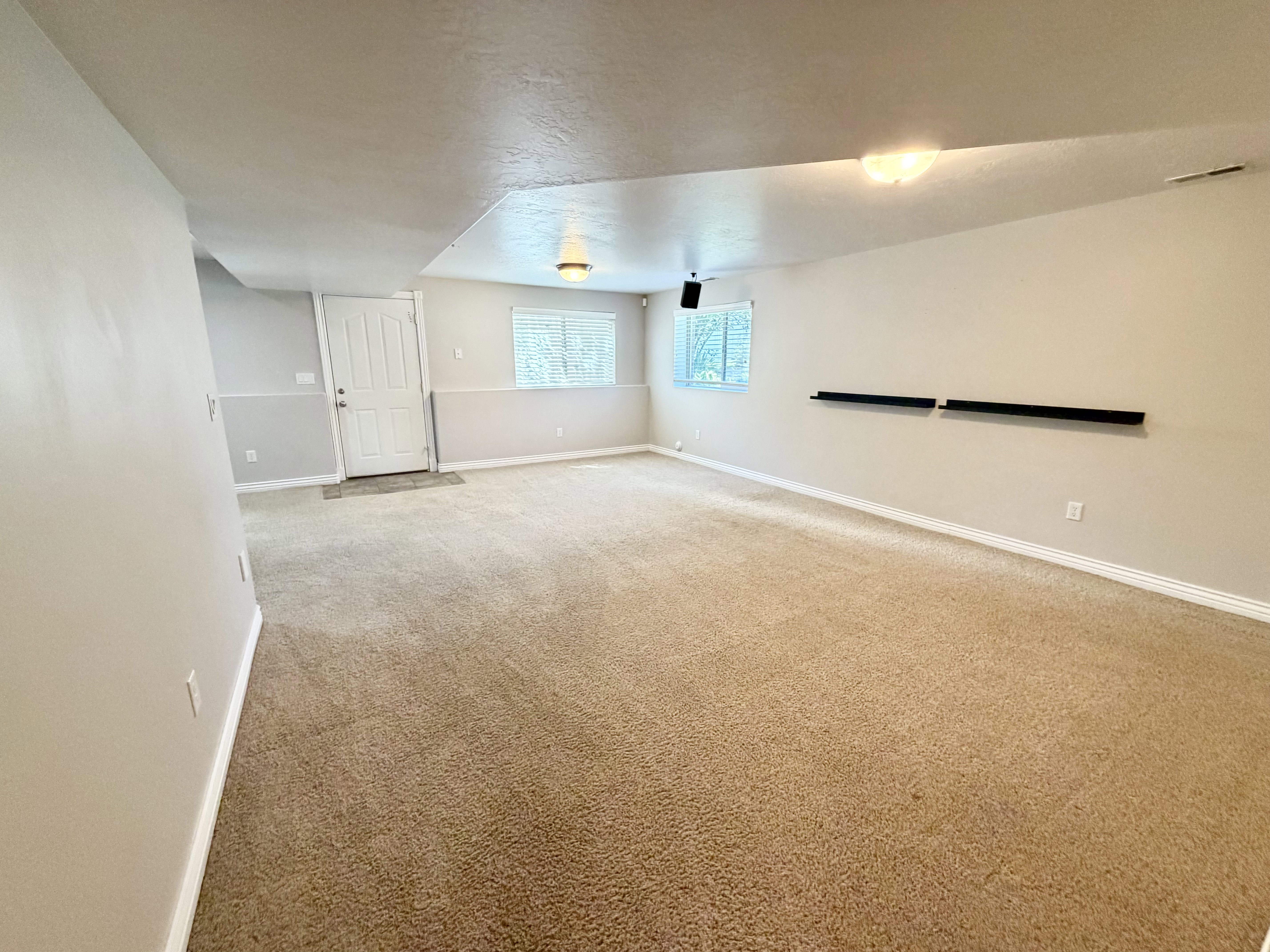 Expansive carpeted room featuring a white paneled door, multiple windows, neutral wall tones, and recessed lighting