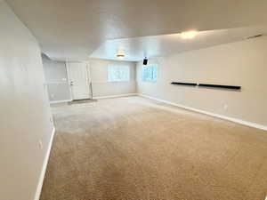 Expansive carpeted room featuring a white paneled door, multiple windows, neutral wall tones, and recessed lighting