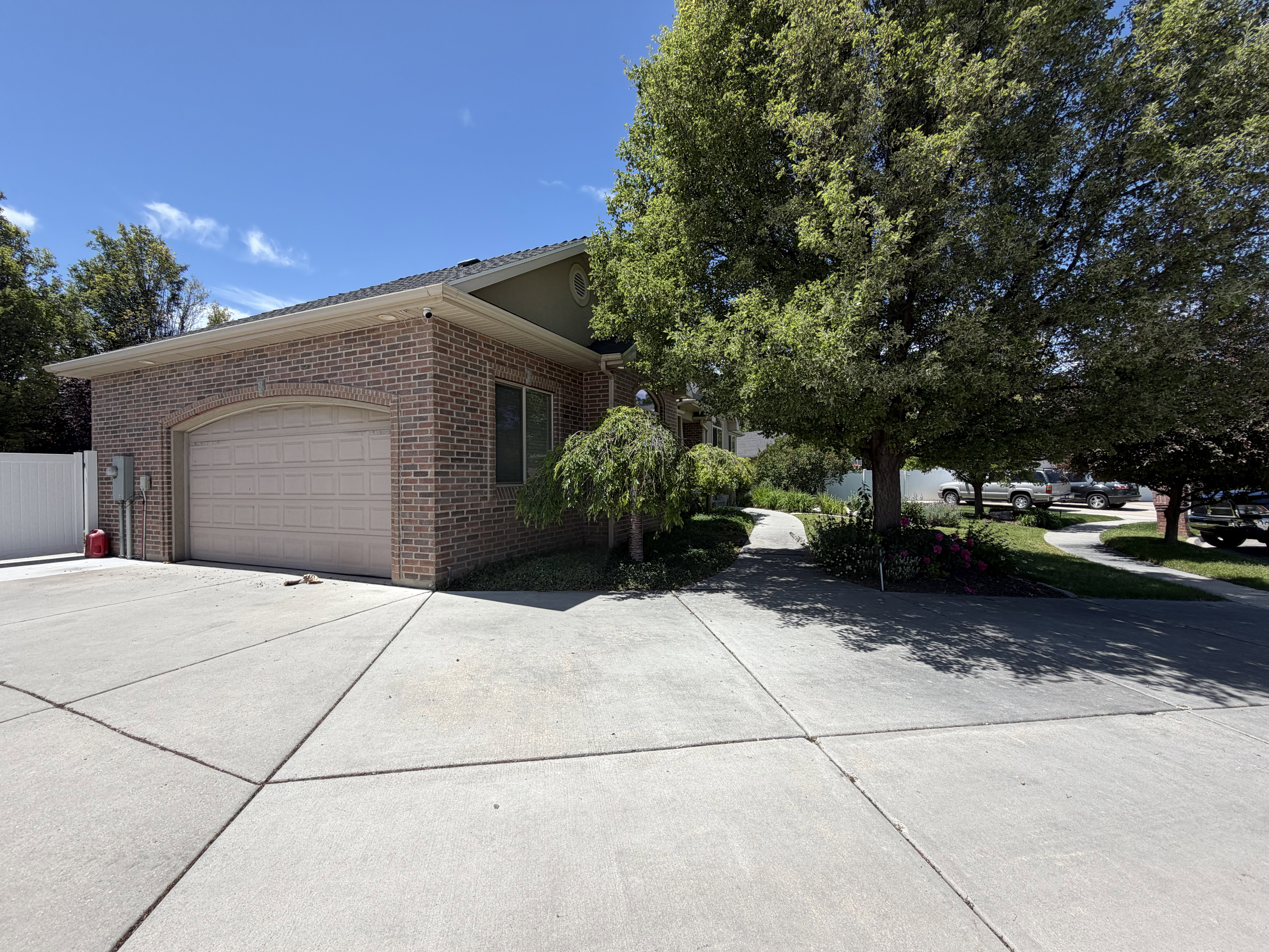 Brick exterior with an arched garage door, concrete driveway, and mature landscaping