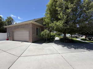 Brick exterior with an arched garage door, concrete driveway, and mature landscaping