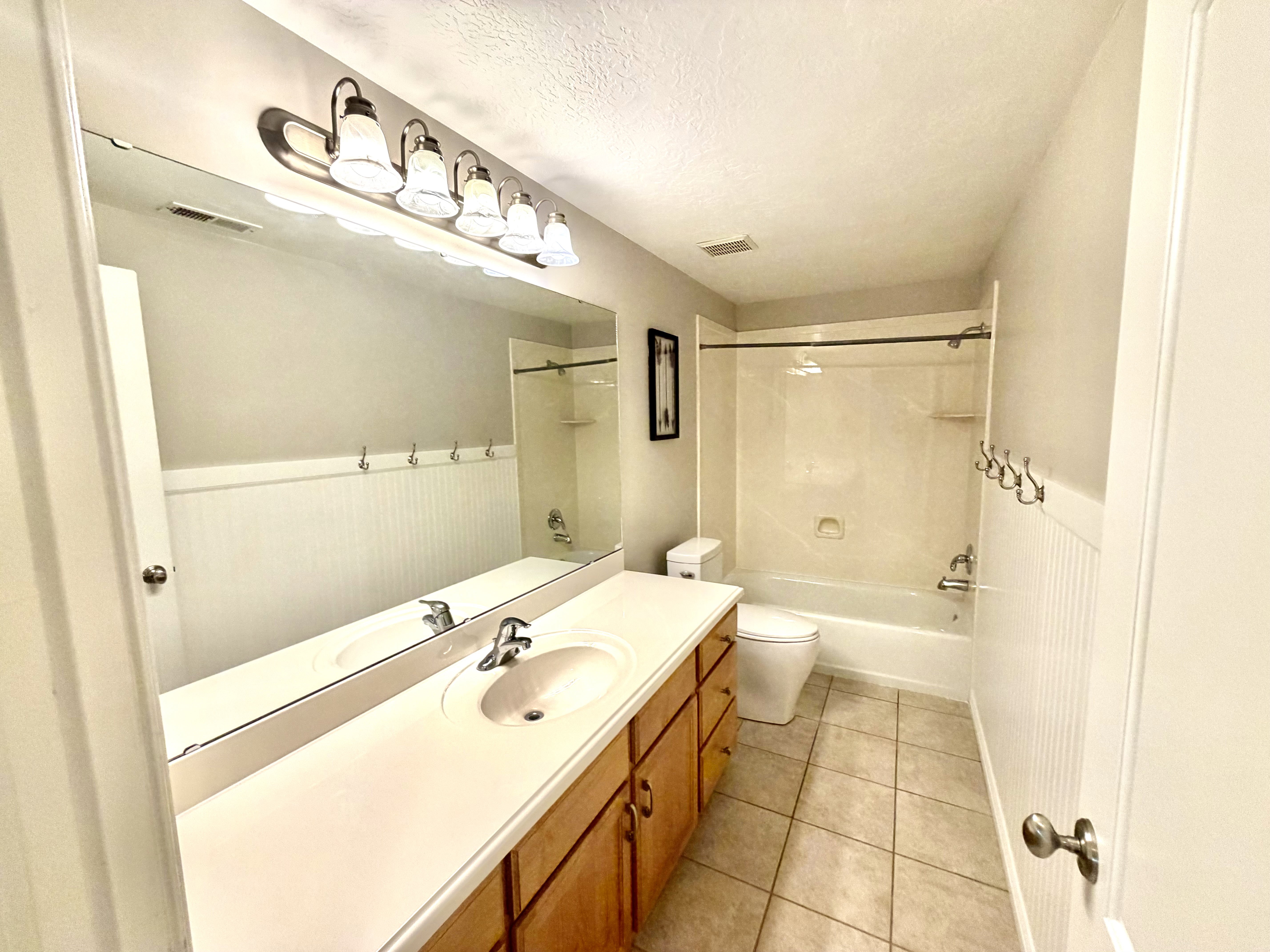 Bathroom featuring a single vanity with a laminate countertop, wood-finish cabinetry, a built-in bathtub with shower, beadboard wainscoting, and tile flooring