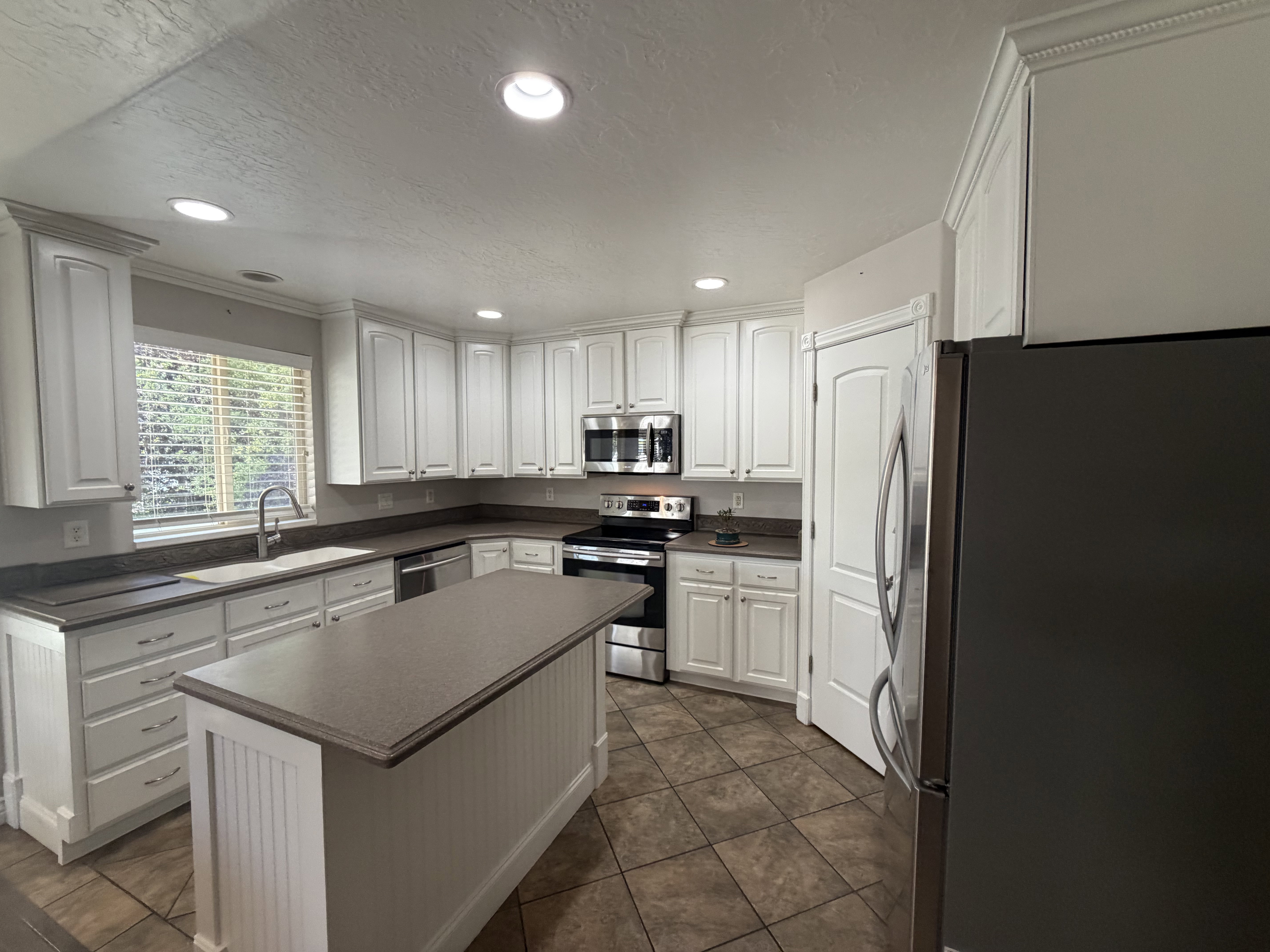 Kitchen featuring a central island with beadboard paneling, white cabinetry with crown molding, stainless steel appliances, a deep single-basin sink with a gooseneck faucet, and earth-toned tile flooring