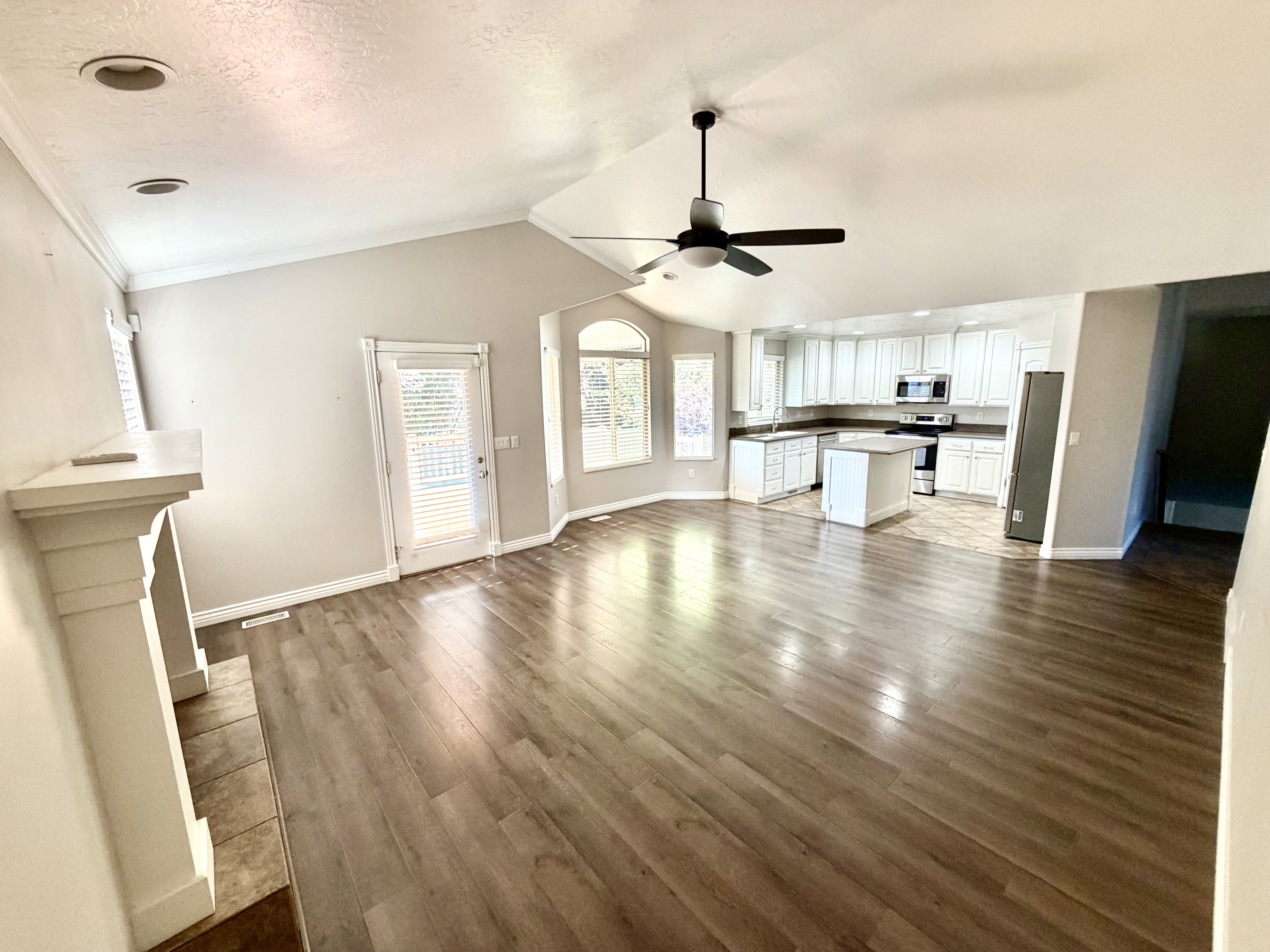 Open-concept living area featuring wood-finish flooring, a vaulted ceiling, and a fireplace with a mantel
