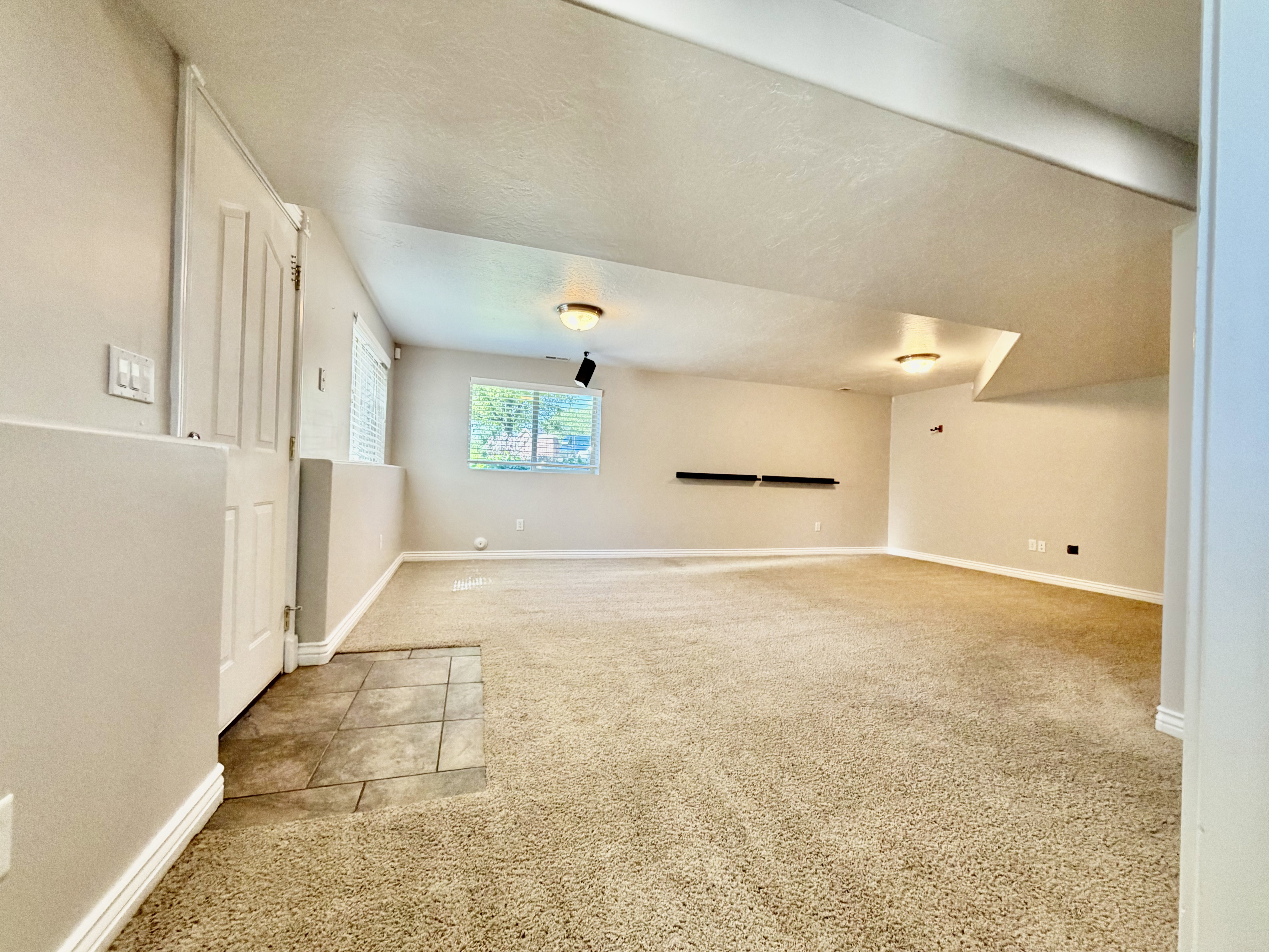 Spacious room featuring neutral carpeting, recessed ceiling lighting, and a window with blinds