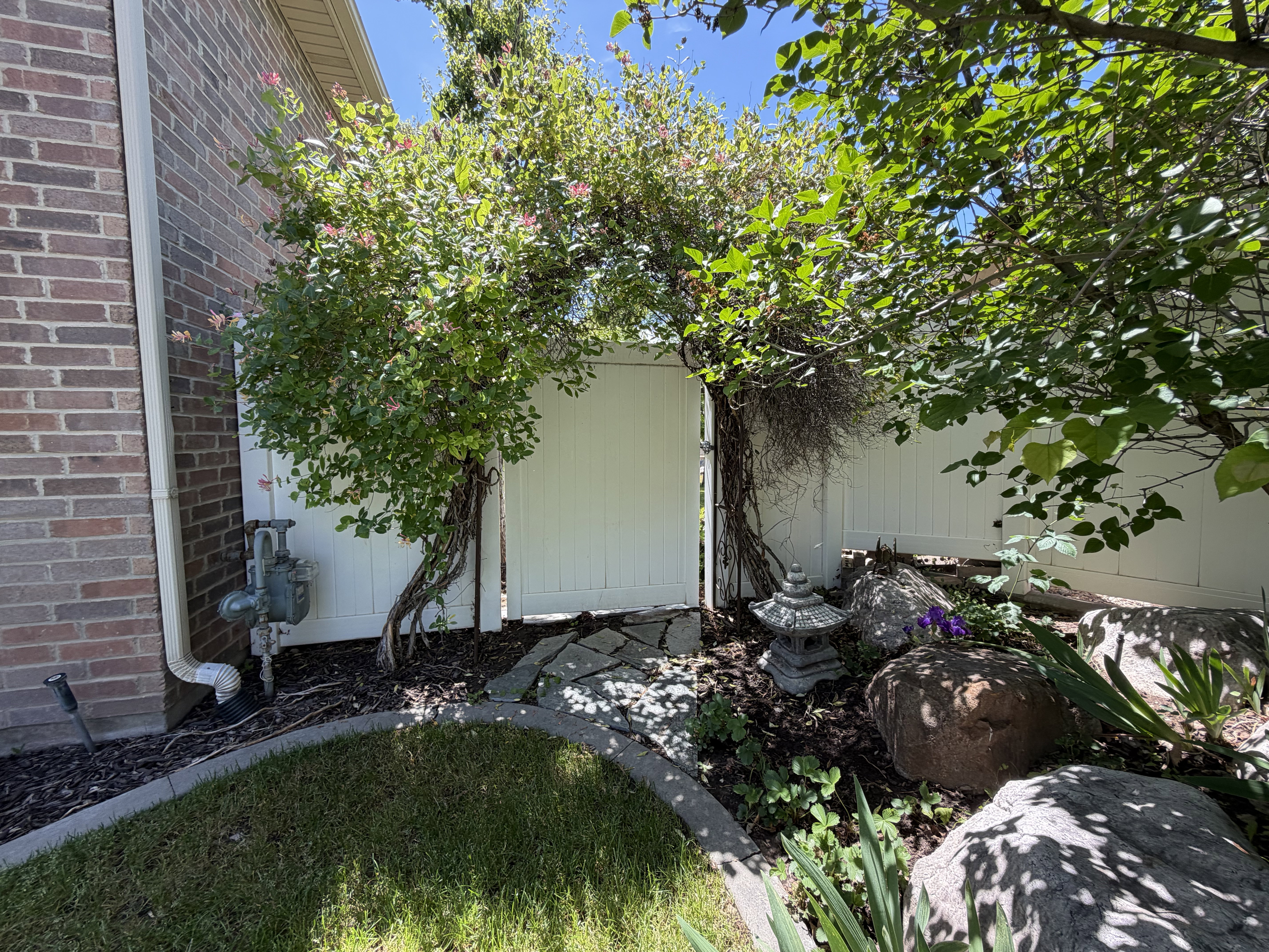 Garden gate with stone pathway, framed by mature plantings and a brick exterior