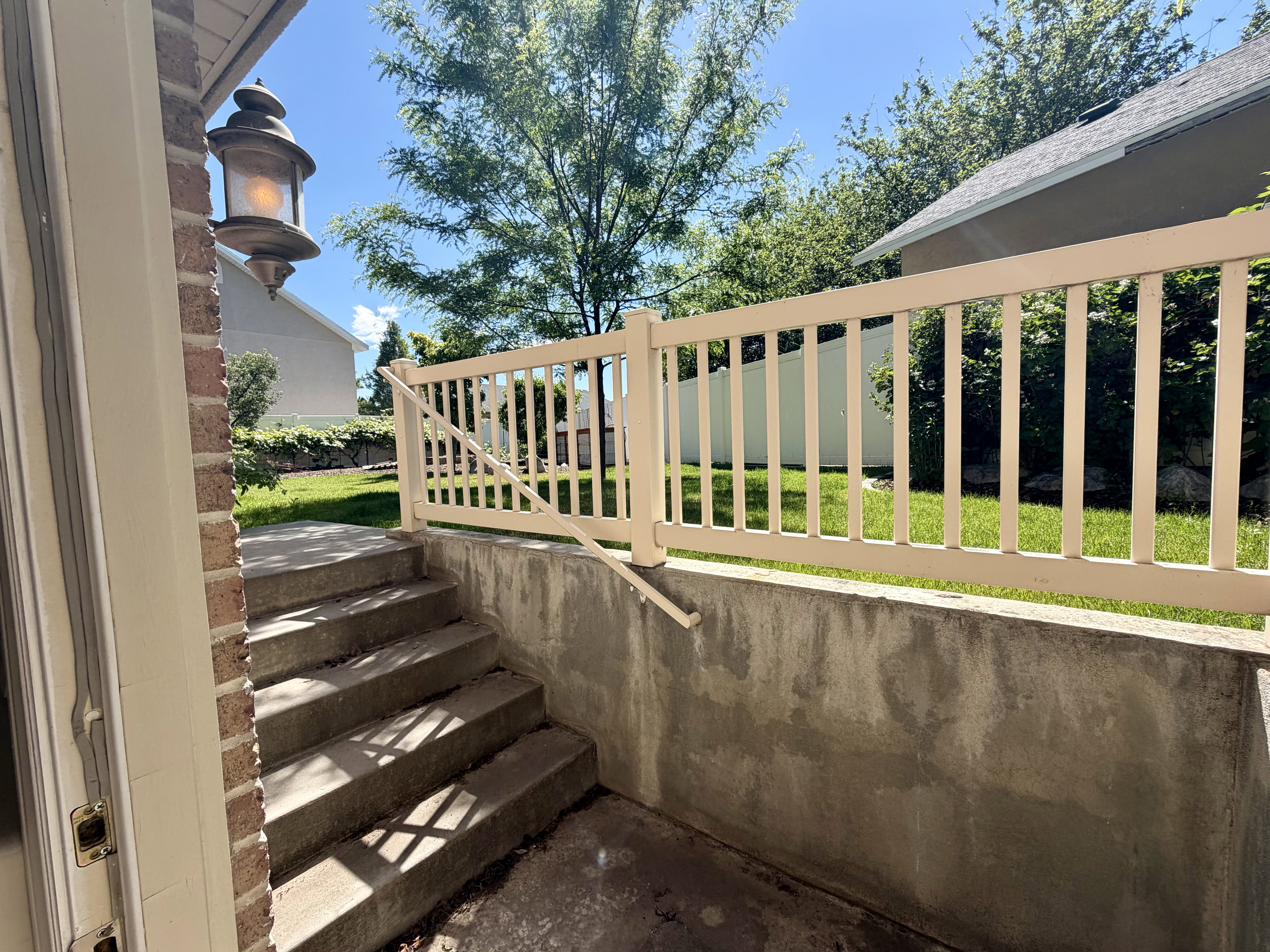 Exterior concrete staircase with a white railing and handrail, leading to a green lawn with perimeter fencing