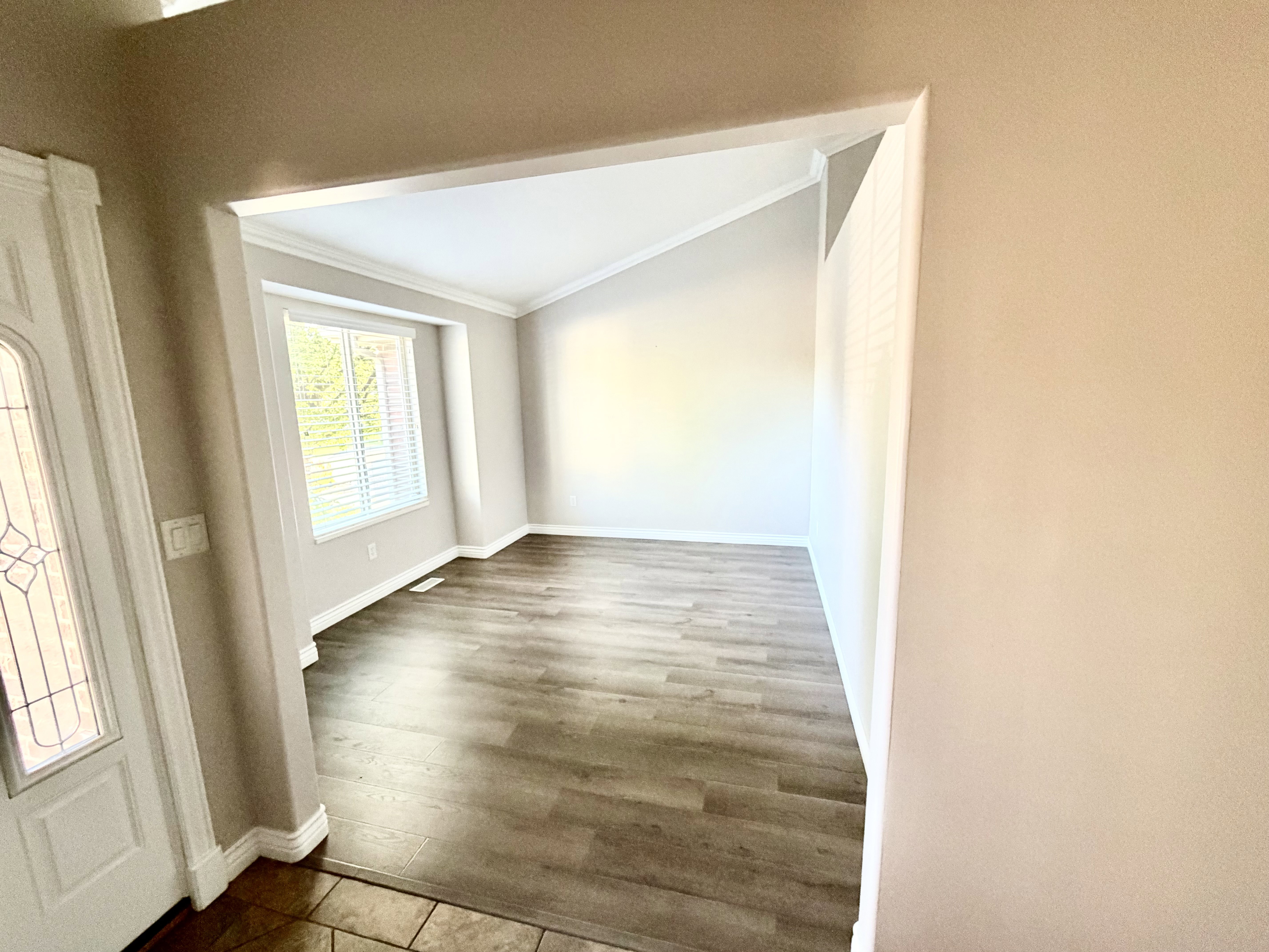 Spacious interior room featuring wood-finish flooring, white baseboards, and a large window with horizontal blinds