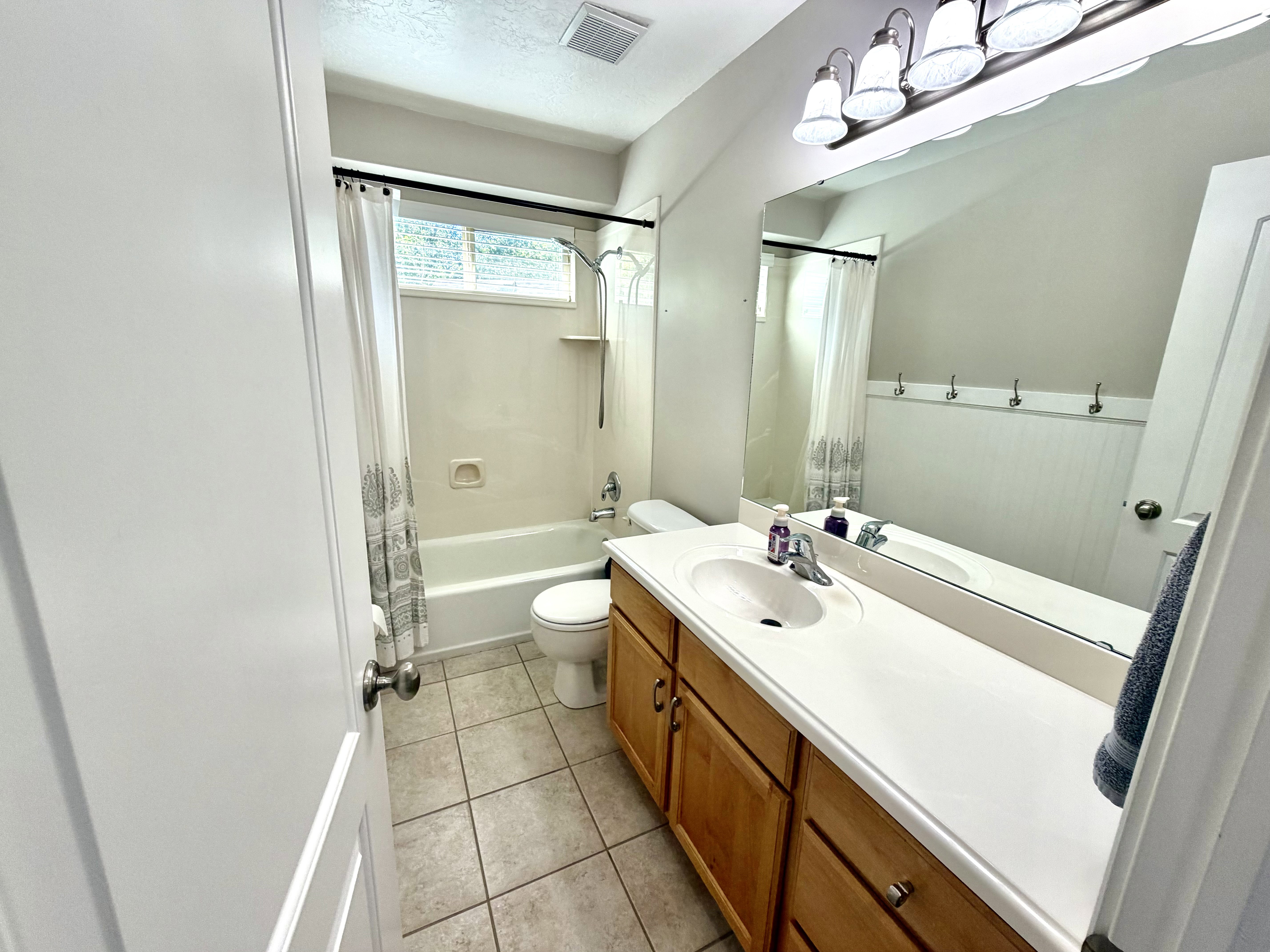 Bathroom featuring a wood-finish vanity with a white countertop and integrated sink, ceramic tile flooring, and a bathtub with shower