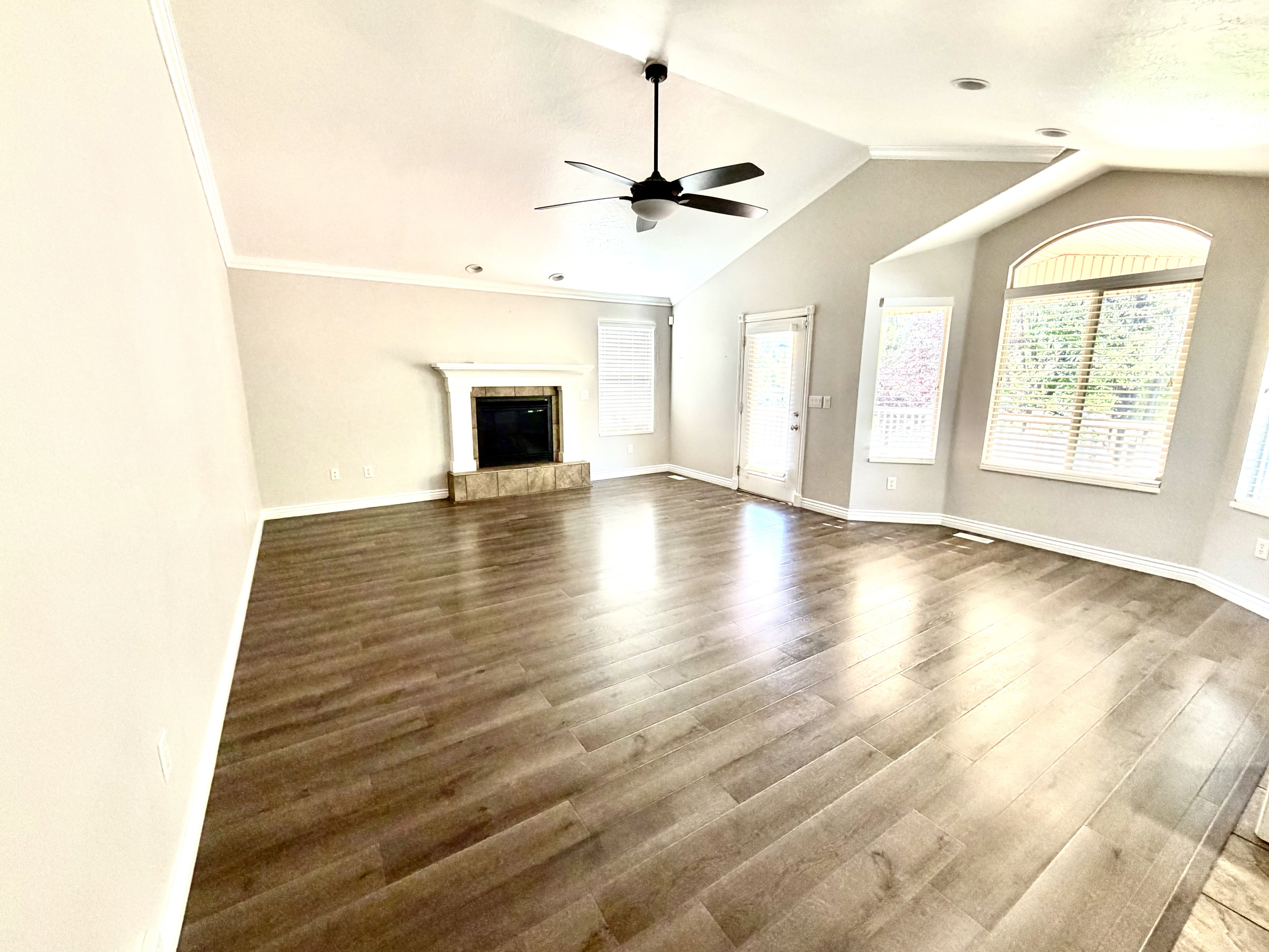 Vaulted ceilings with a ceiling fan, fireplace with a stone surround, wood-finish flooring, recessed lighting, and large bay windows with blinds