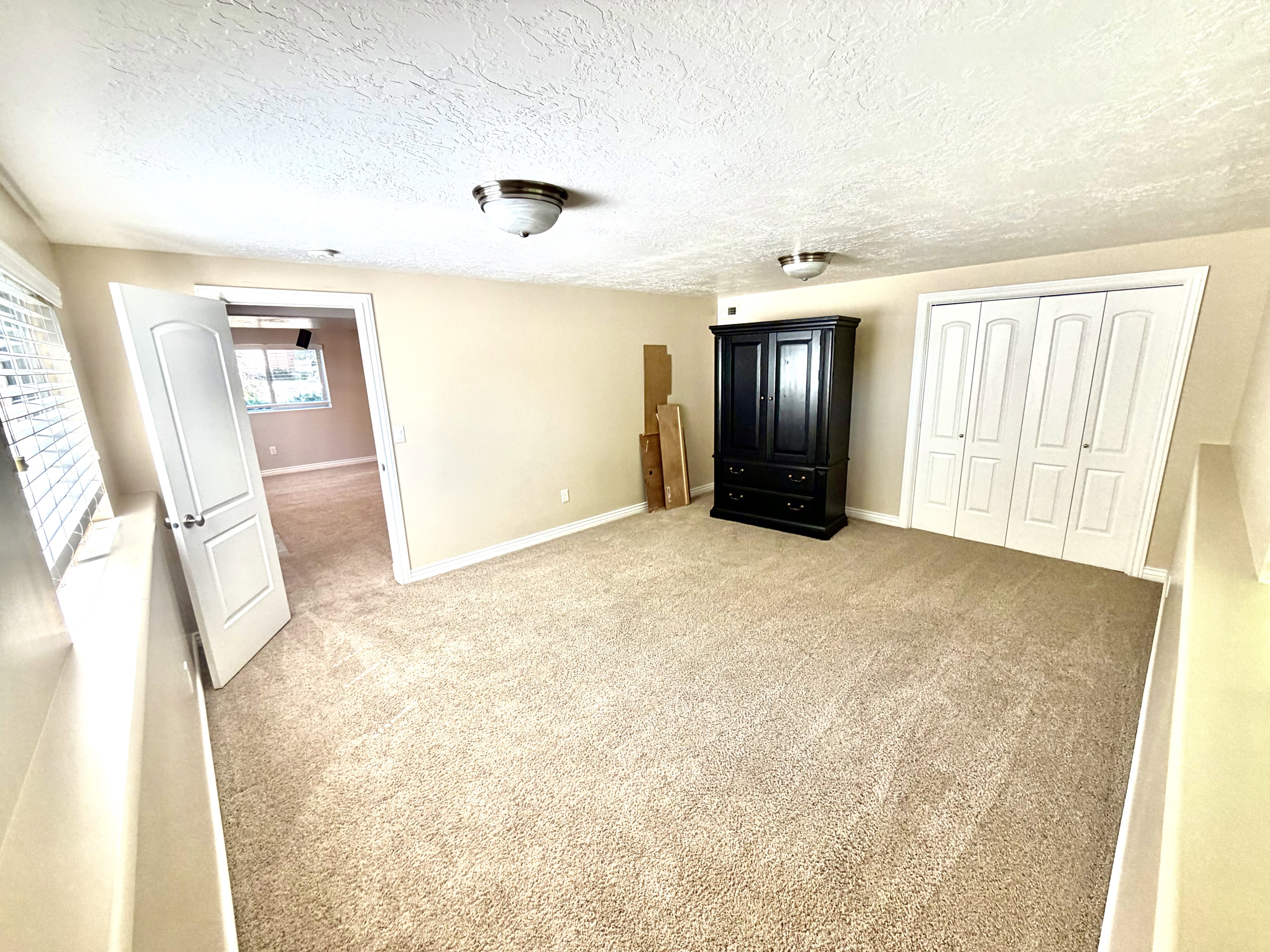 Carpeted room featuring a white paneled door, a window with horizontal blinds, and bi-fold closet doors