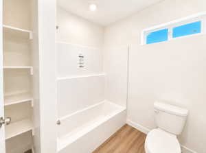 Bathroom featuring a white tub-shower combination with chrome fixtures, a white toilet, and wood-finish flooring