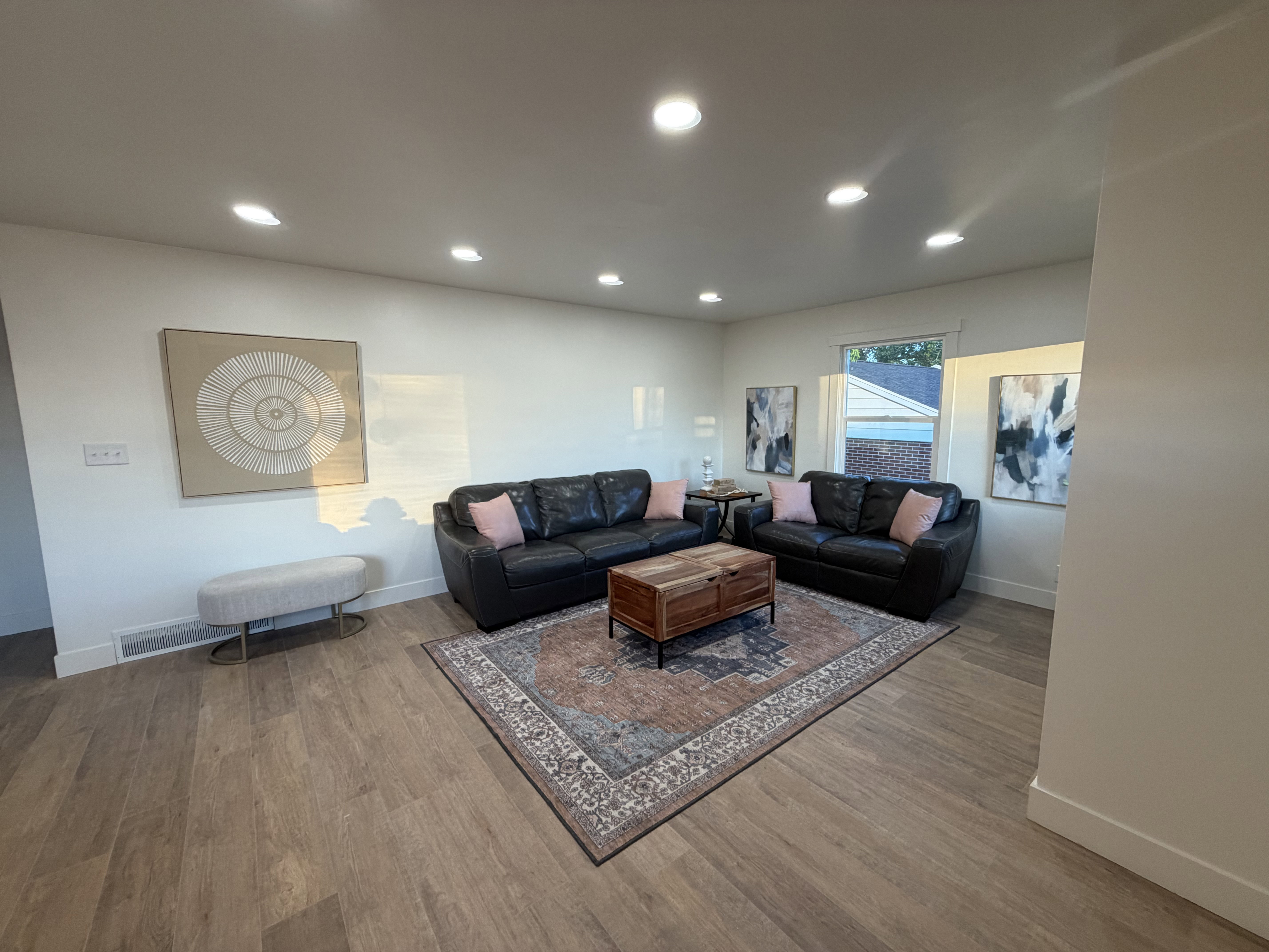Spacious living area featuring light wood-finish flooring, recessed ceiling lighting, and crisp white walls