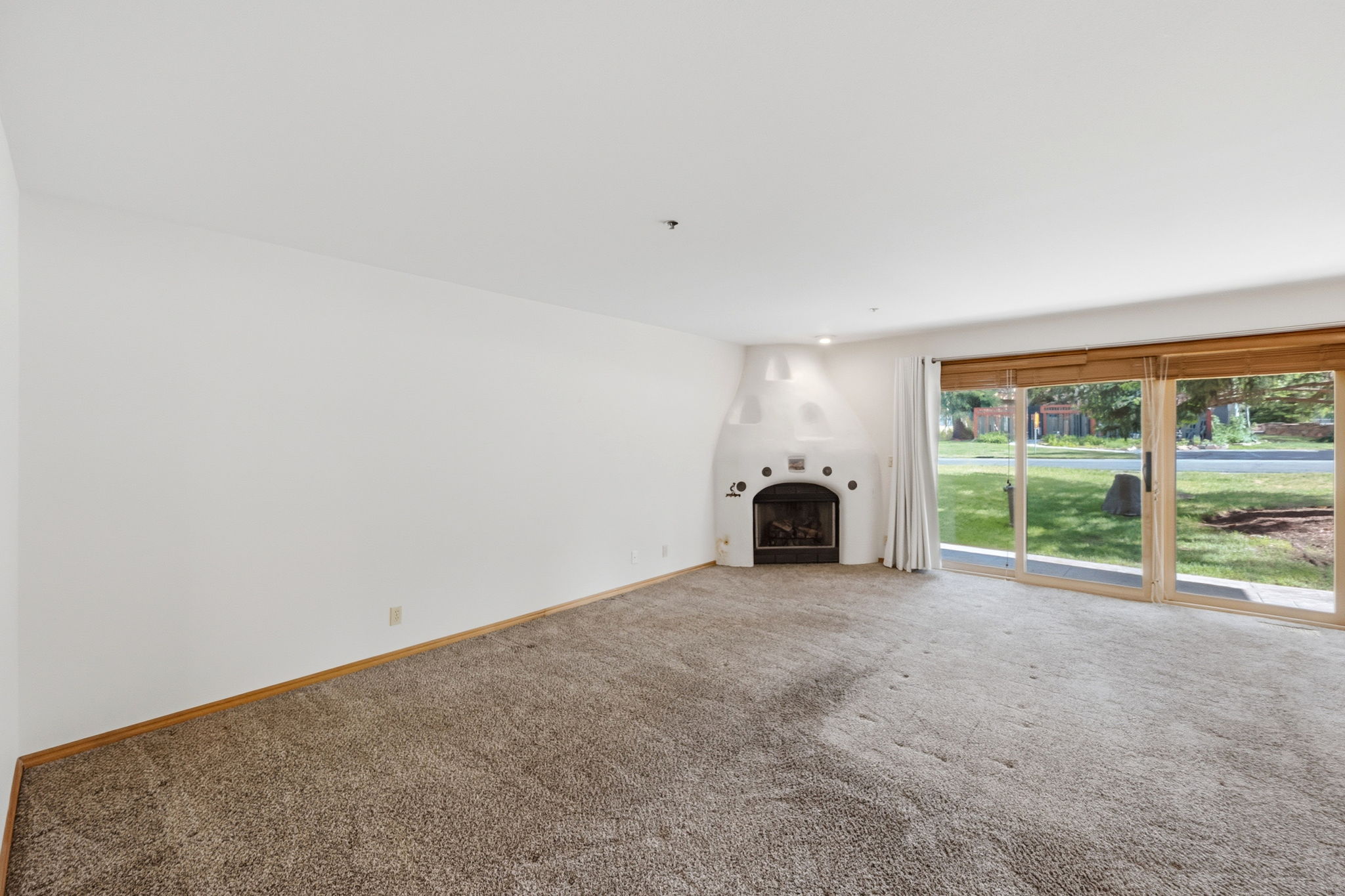Living area featuring a kiva fireplace, broad sliding glass doors, white walls, and neutral carpeting