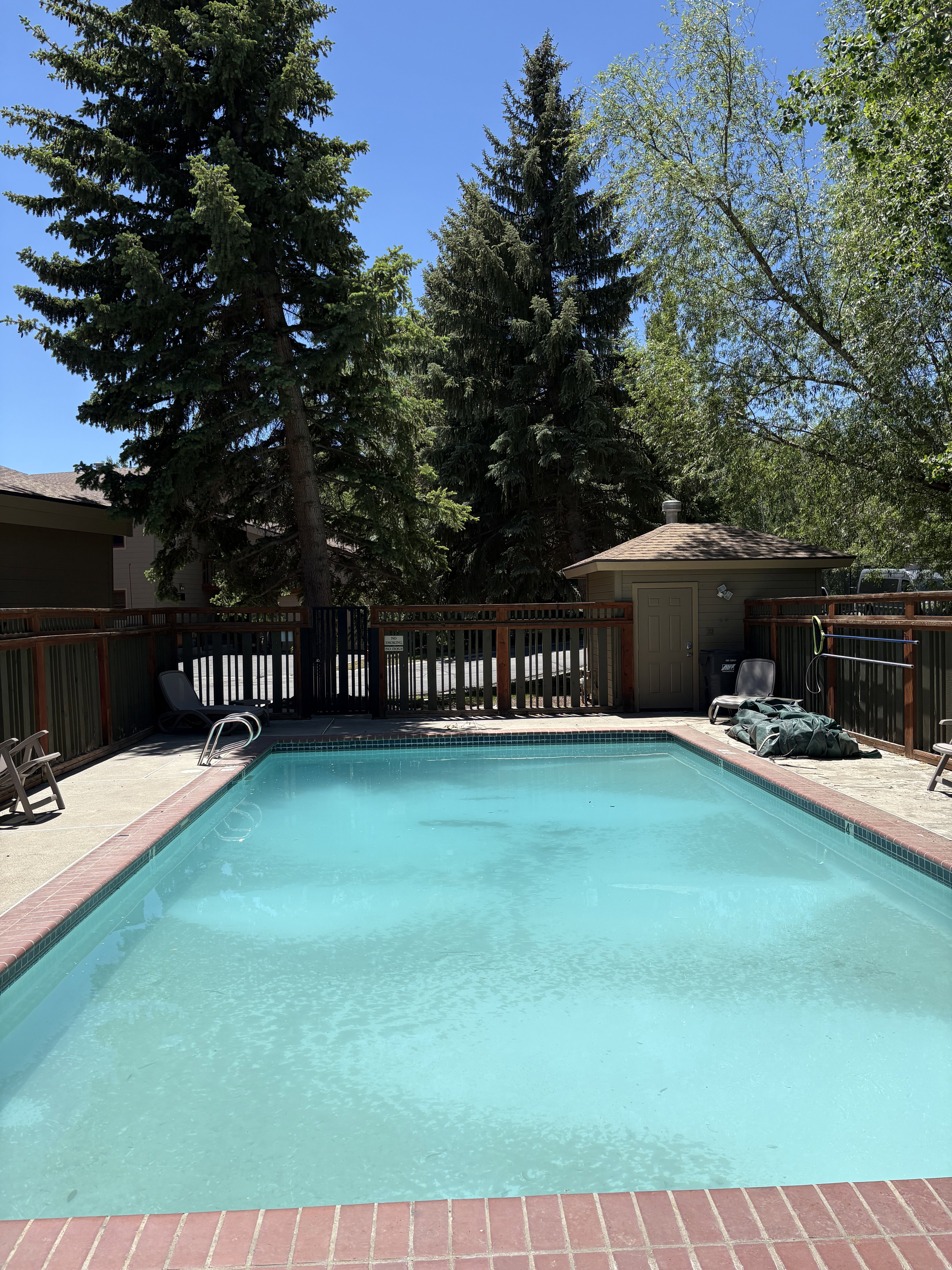 Outdoor swimming pool with brick coping, surrounding hardscaping, and a wooden perimeter fence