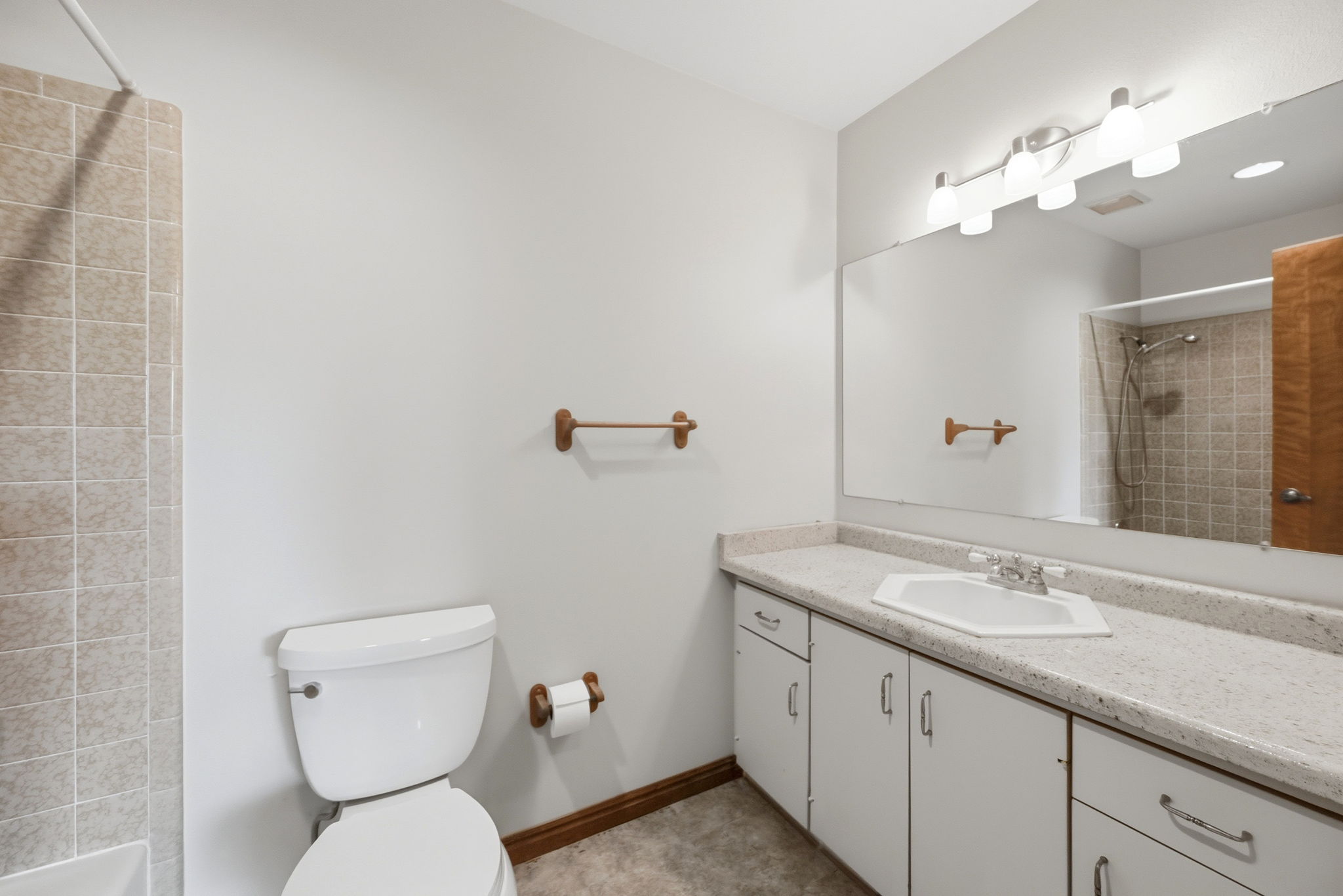 Bathroom featuring a shower with light-toned square tile surround, white toilet, and a vanity with a white countertop and integrated hexagonal sink