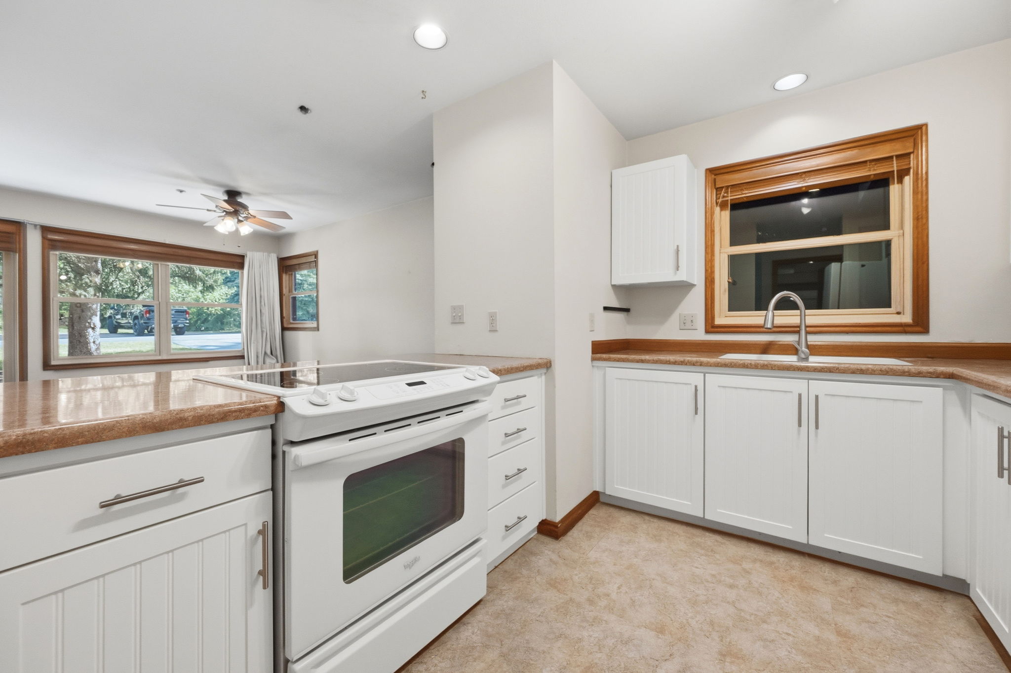 Kitchen featuring white cabinetry, light-toned countertops, a built-in electric range, a stainless steel sink with a gooseneck faucet, and tile flooring