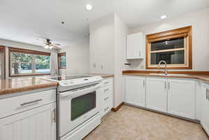 Kitchen featuring white cabinetry, light-toned countertops, a built-in electric range, a stainless steel sink with a gooseneck faucet, and tile flooring
