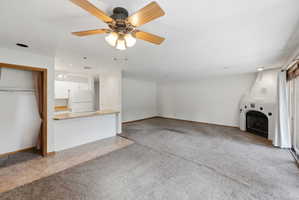Living area featuring a textured carpet, a kiva-style fireplace, and a ceiling fan with integrated lighting