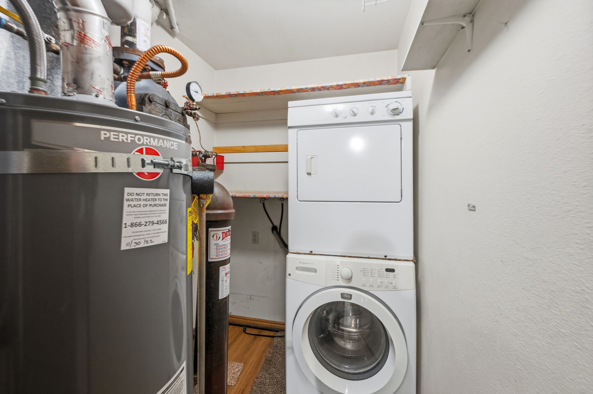 Utility area featuring a water heater, stacked washer and dryer, and wall-mounted shelving