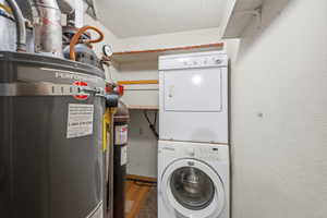 Utility area featuring a water heater, stacked washer and dryer, and wall-mounted shelving