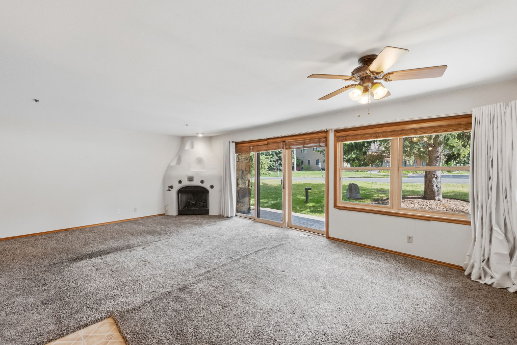 Living area featuring a southwestern-style fireplace, ceiling fan with integrated lighting, expansive windows with wood trim, and glass sliding doors