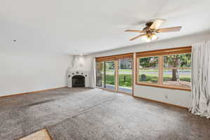 Living area featuring a southwestern-style fireplace, ceiling fan with integrated lighting, expansive windows with wood trim, and glass sliding doors
