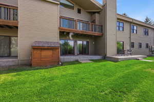 Rear exterior featuring a vibrant green lawn, two concrete patios, two sets of sliding glass doors. Additional storage closet off the porch.