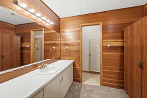 Bathroom featuring extensive wood paneling, a full vanity with an integrated sink, a large mirror with strip lighting, and a separate shower area