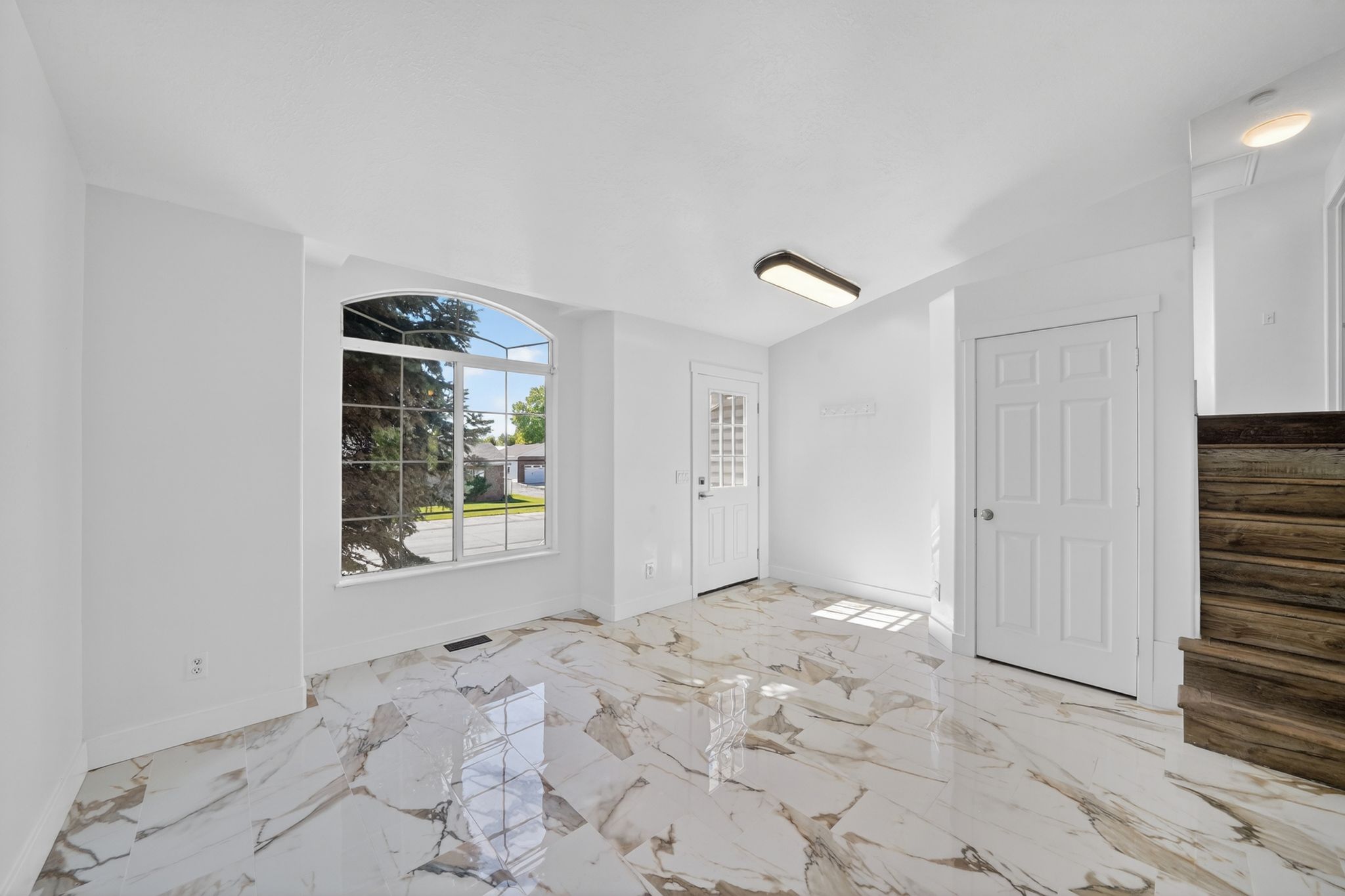 Entry area featuring polished tile flooring, an arched picture window, a solid panel door, and exposed wood-finish stairs