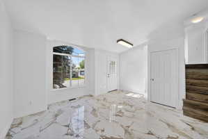 Entry area featuring polished tile flooring, an arched picture window, a solid panel door, and exposed wood-finish stairs