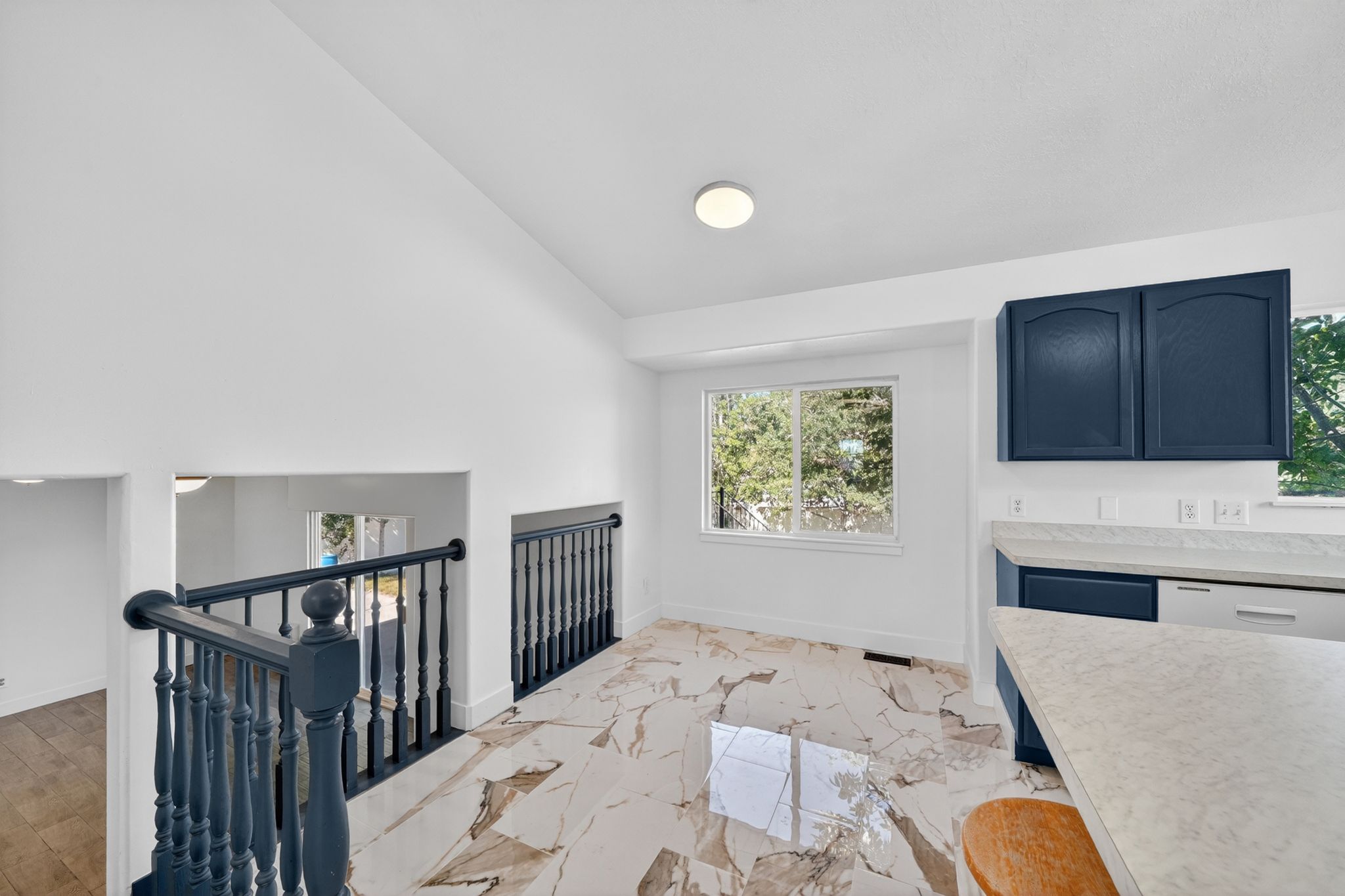 Open concept living area featuring high vaulted ceilings, light-tone marble-finish flooring, and a modern kitchen with blue cabinetry and light-tone countertops