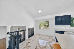 Open concept living area featuring high vaulted ceilings, light-tone marble-finish flooring, and a modern kitchen with blue cabinetry and light-tone countertops