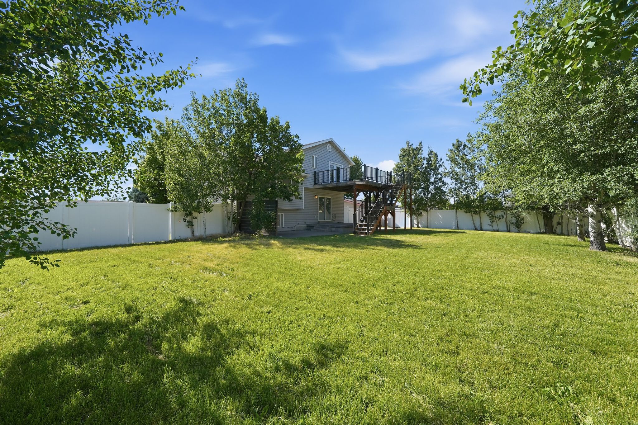 Expansive grassy yard enclosed by a privacy fence, featuring mature perimeter trees