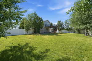 Expansive grassy yard enclosed by a privacy fence, featuring mature perimeter trees