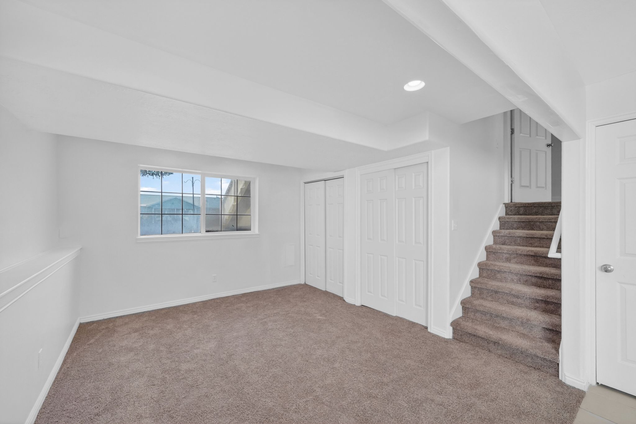 Spacious carpeted room featuring a large grid-pattern window, recessed lighting, and white bi-fold closet doors