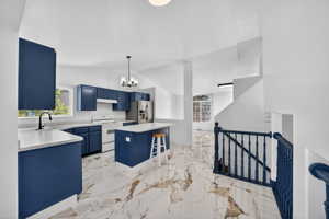 Bright kitchen featuring blue cabinetry, white countertops, a central island, stainless steel appliances, and large-format tile flooring