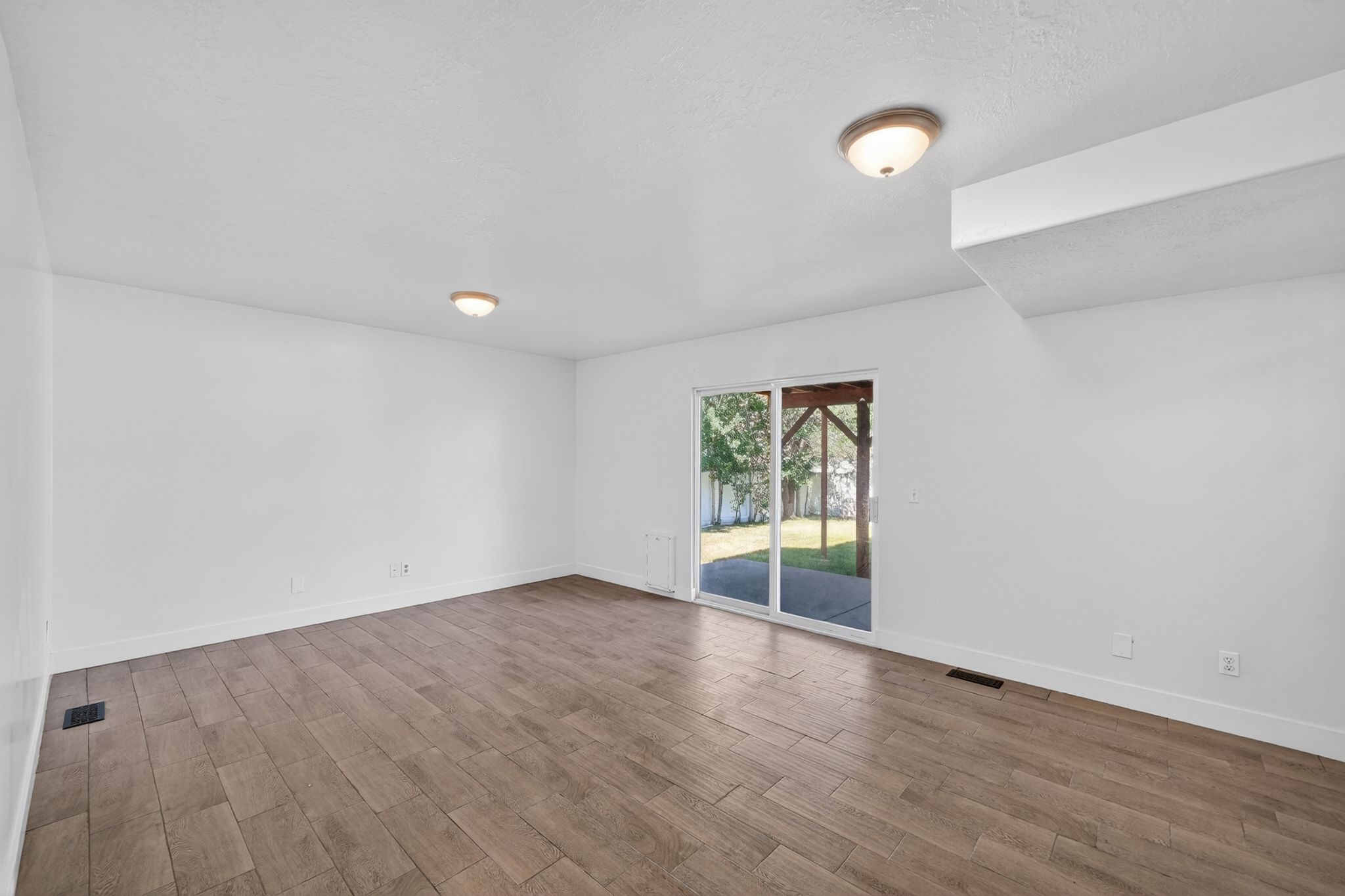 Spacious room featuring wood-finish flooring, white walls, and a sliding glass door leading to an outdoor patio area