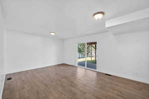 Spacious room featuring wood-finish flooring, white walls, and a sliding glass door leading to an outdoor patio area