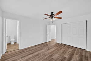 Spacious room featuring wood-finish flooring, white walls, and a ceiling fan with light fixture